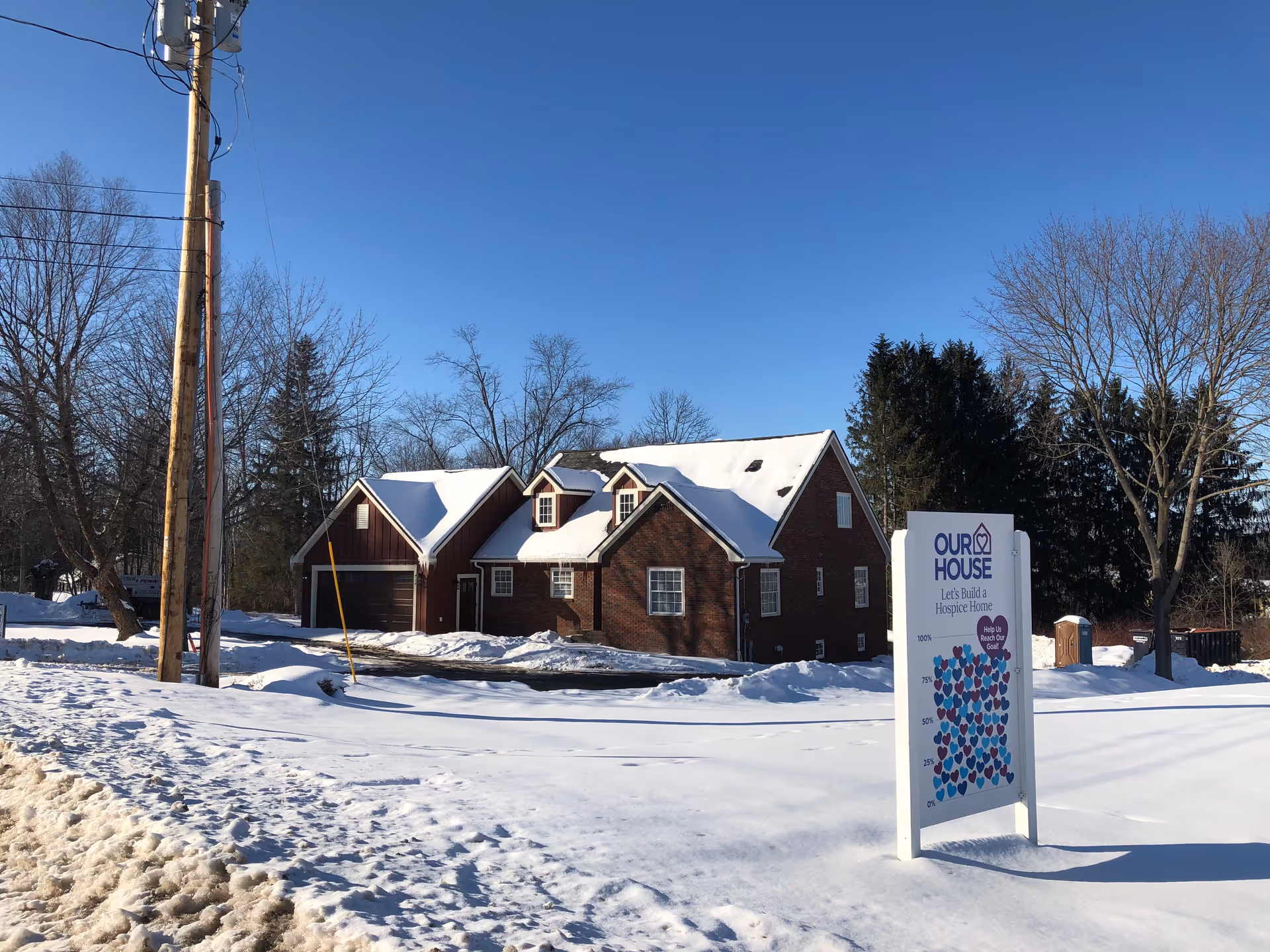 Snow-covered brick building with a sign reading Our House Hospice in foreground.