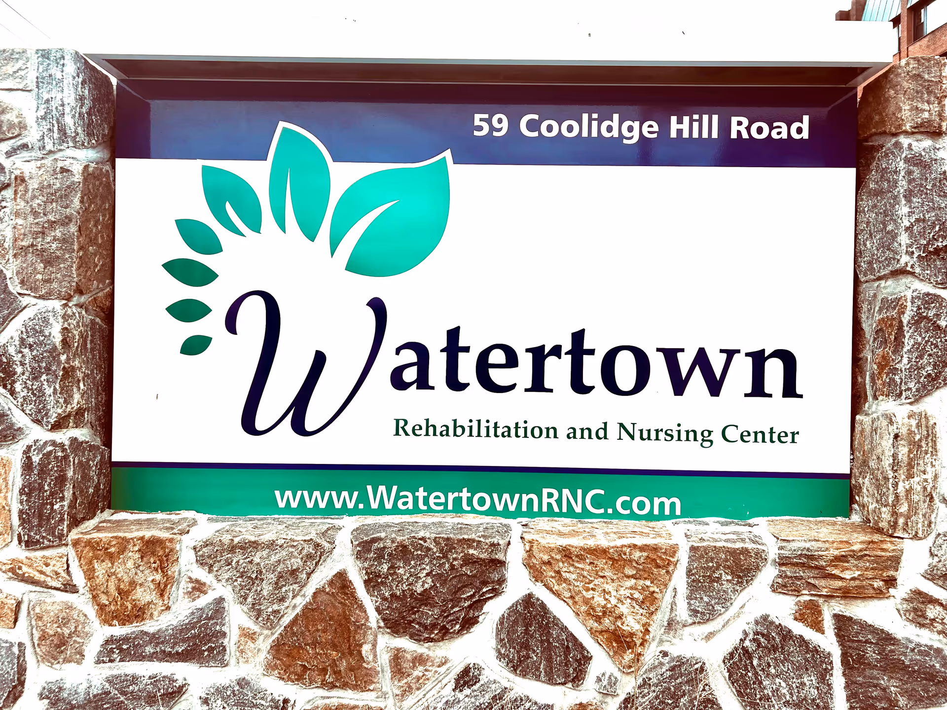 Exterior sign on a stone wall reading Watertown Rehabilitation and Nursing Center.