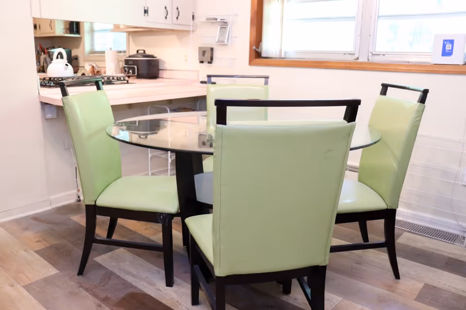 Round glass dining table with four light-green upholstered chairs in a kitchen area.