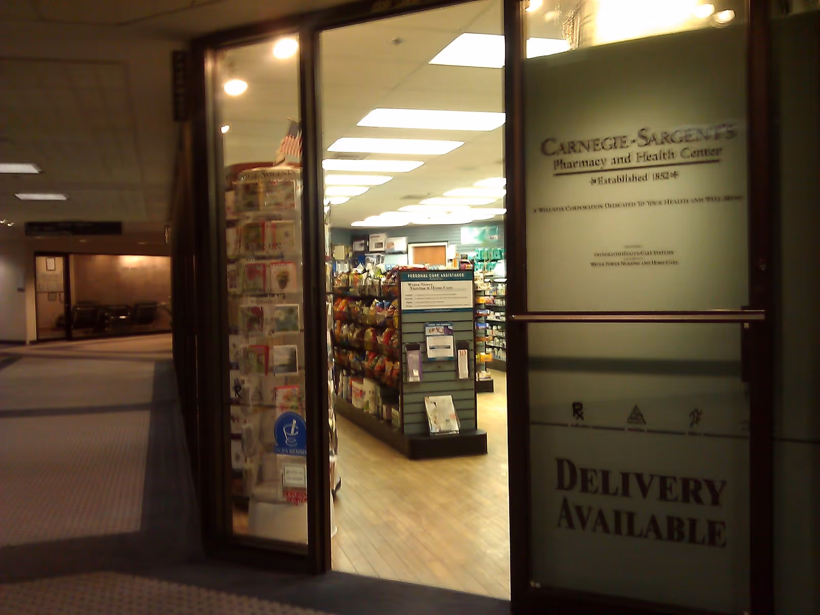 Pharmacy interior inside a senior living facility with shelves and a Delivery Available sign.