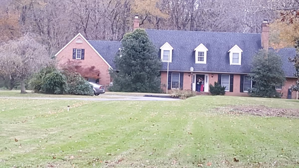 Brick-assisted living facility with a central front entrance, a car, and people by the door.