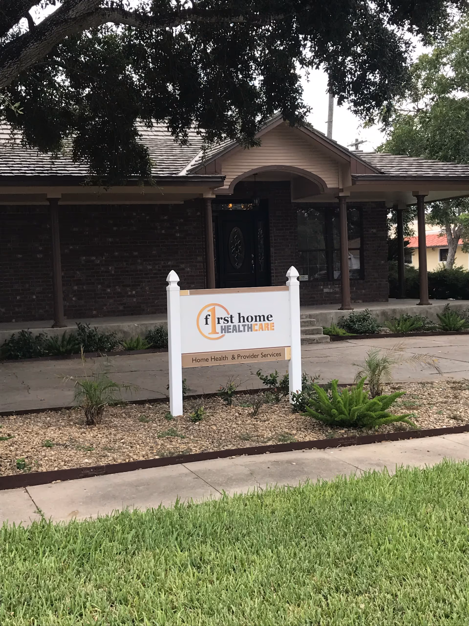 Brick facility with a front porch and a standalone sign reading First Home Healthcare.