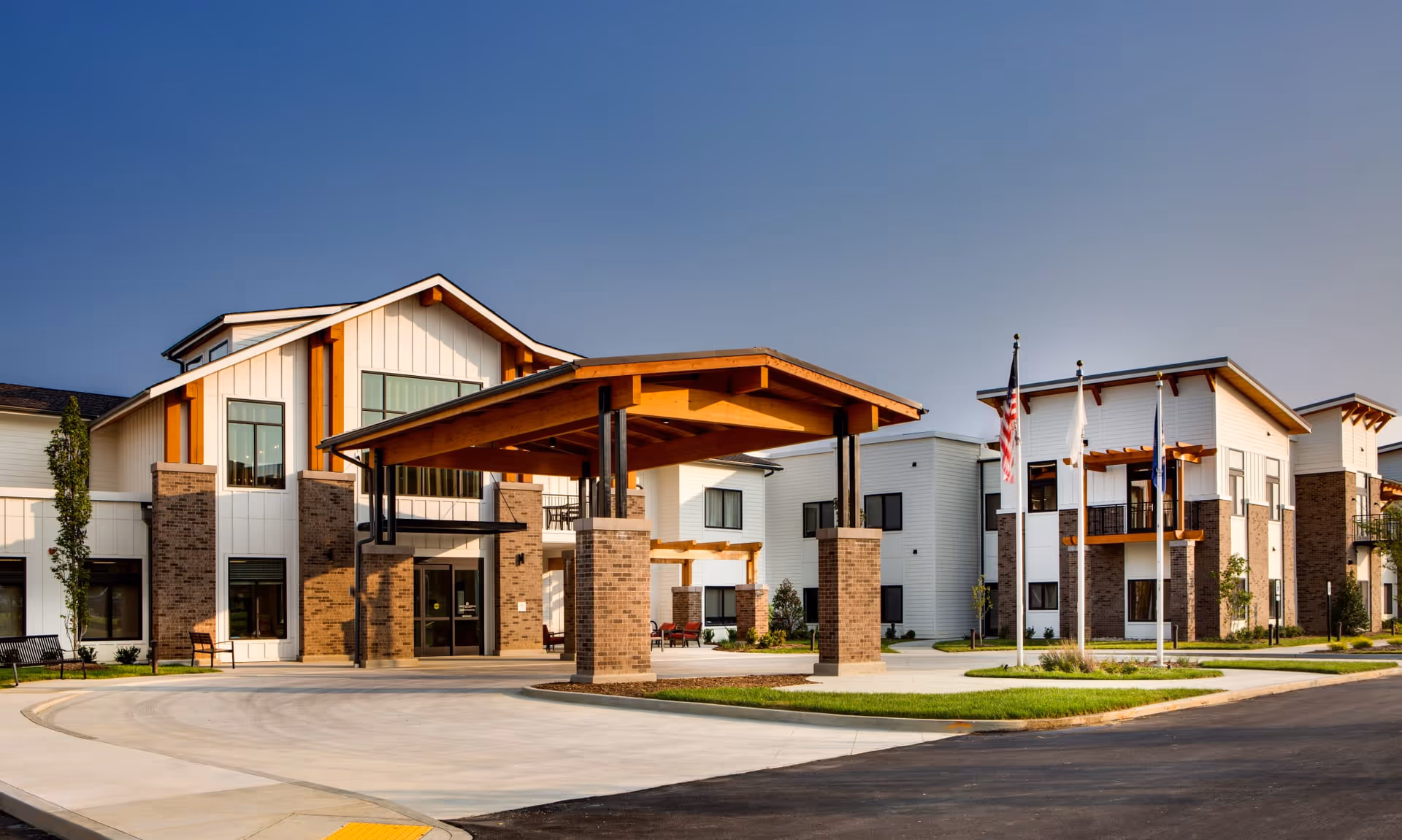 Exterior of Preston Greens Senior Living showing a covered entrance, brick columns, and flagpoles.