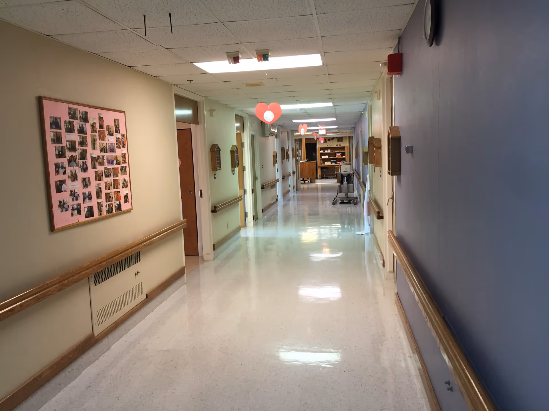 Long bright hallway in a senior living facility with heart decorations and bulletin boards.