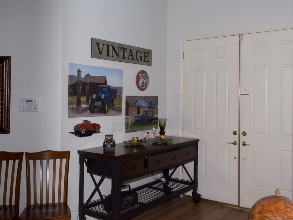 Entryway with a console table topped with decor, vintage wall art, two wooden chairs, and closed double front doors.