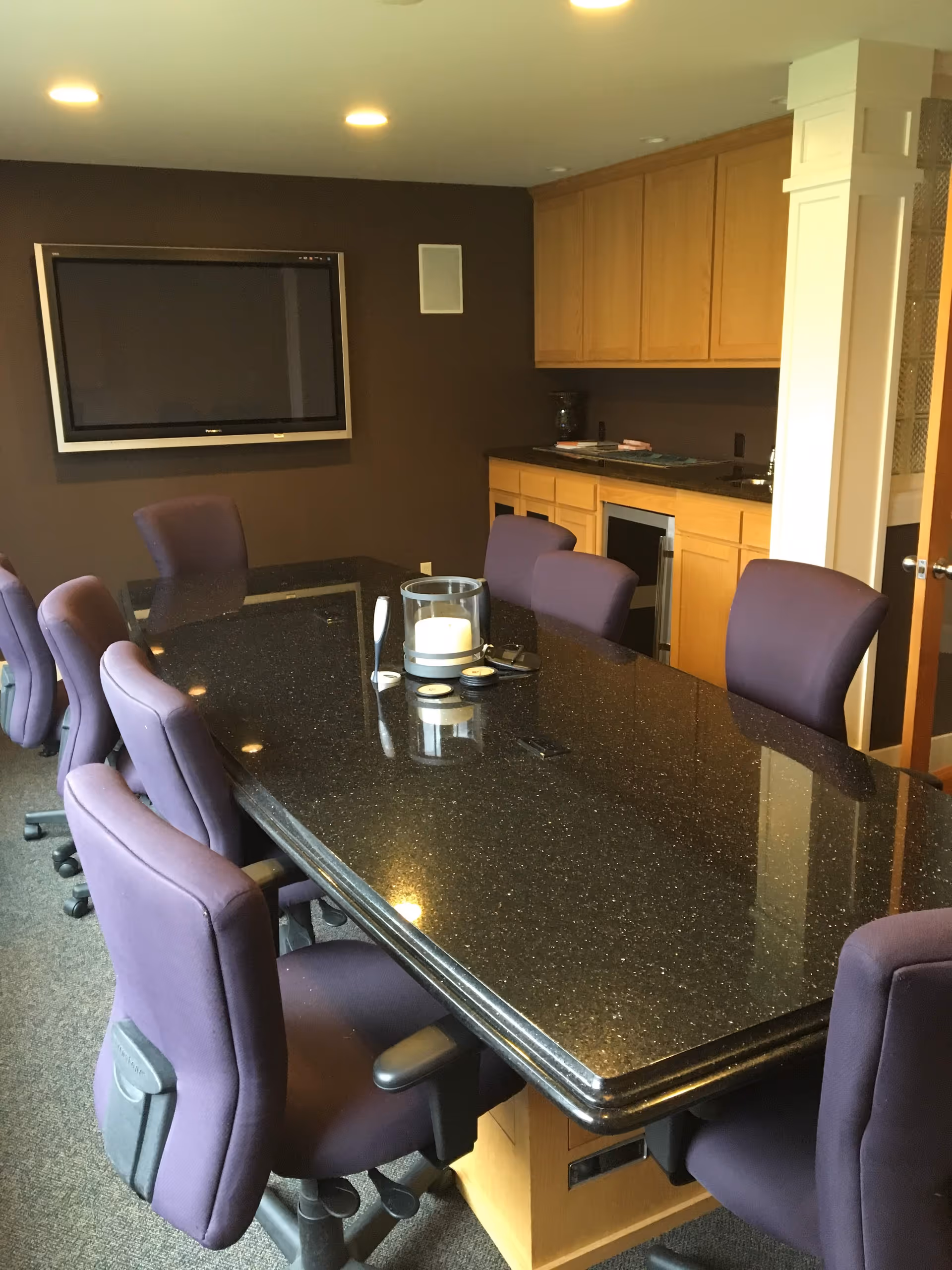 A long dark granite table with purple chairs in a dining room.
