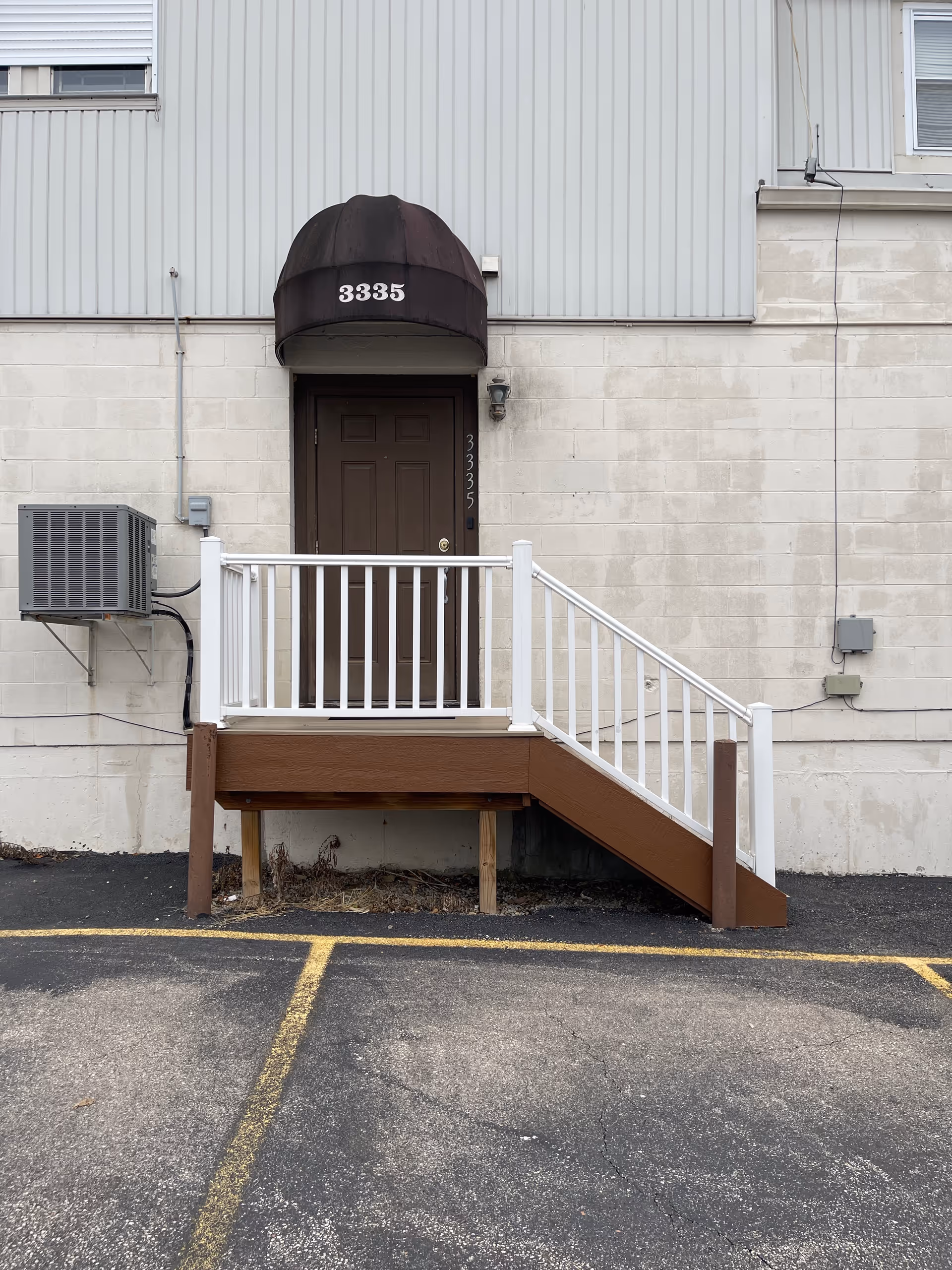 Exterior entrance featuring brown door, brown awning, and white railing stairs.