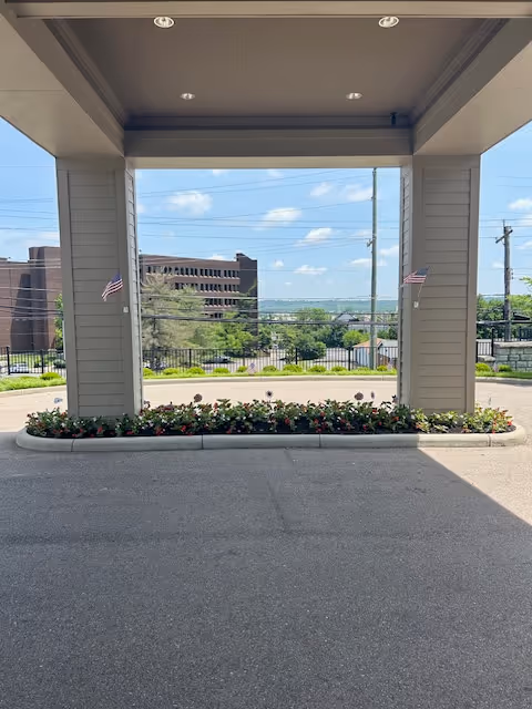 Covered entryway with a flower bed and distant buildings under a blue sky.