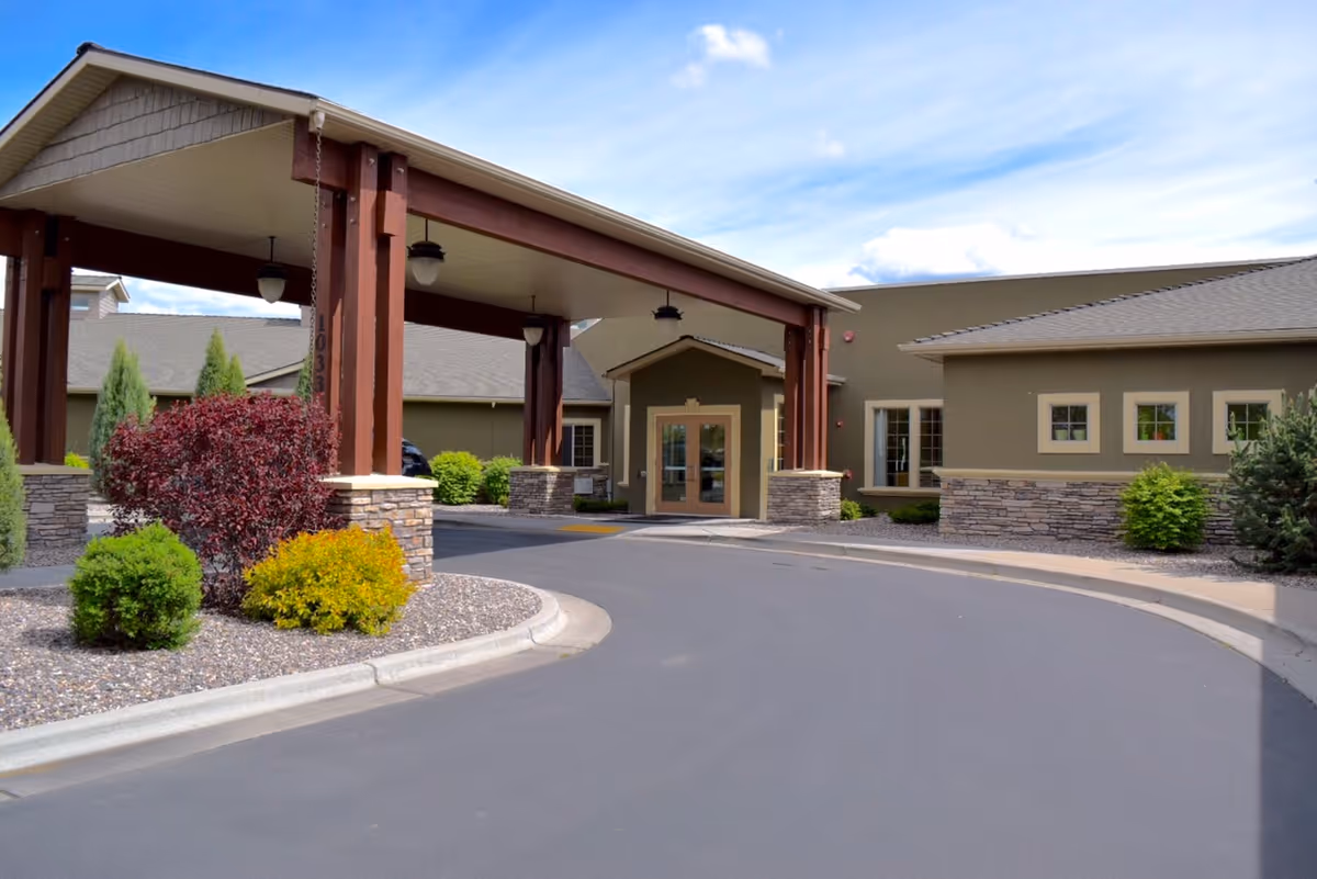 Exterior view of a senior living facility entrance with a covered drop-off and landscaping.