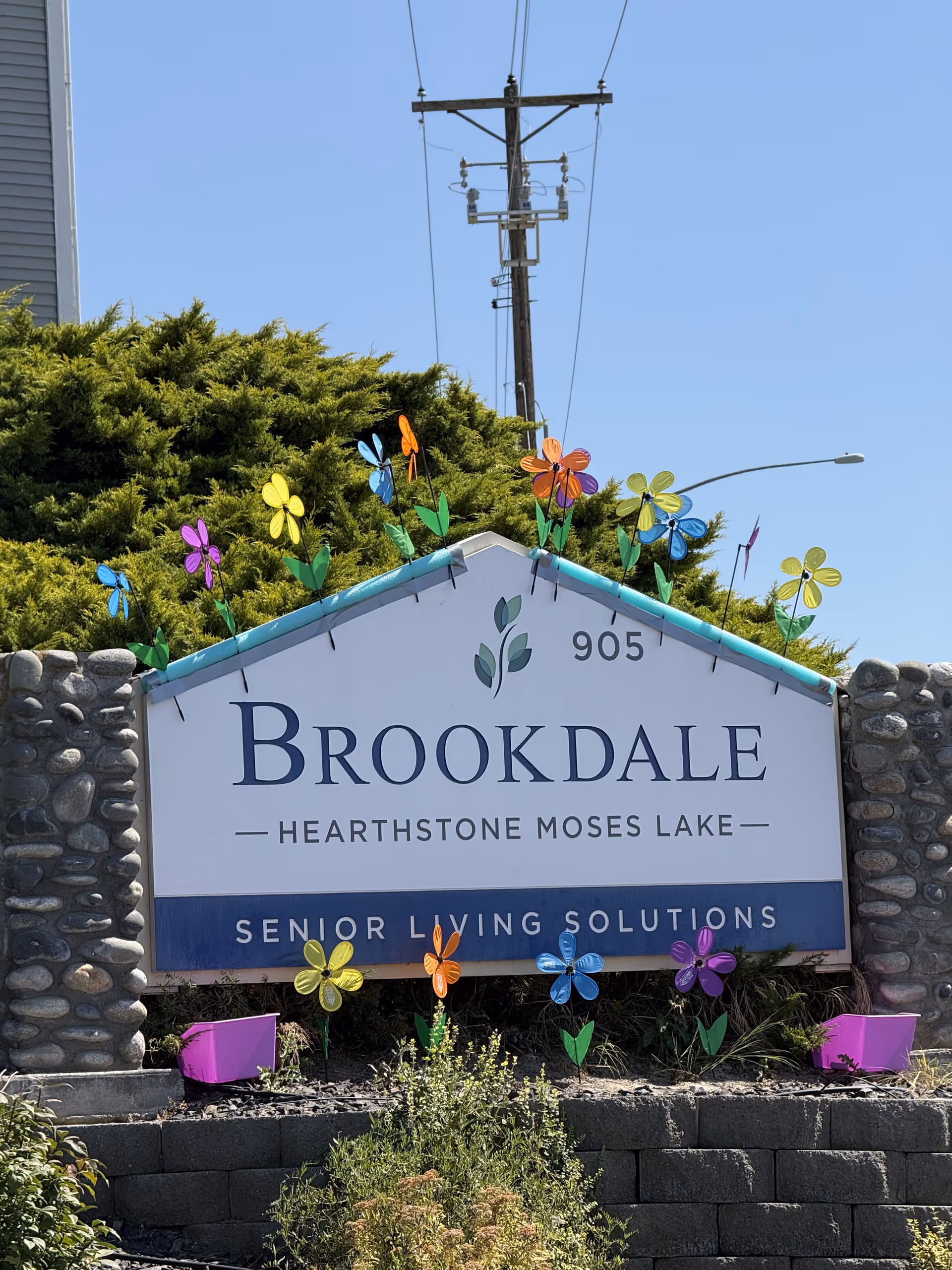 Outdoor sign for Brookdale Hearthstone Moses Lake with colorful pinwheels and stone pillars.