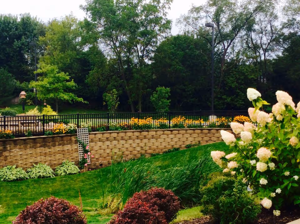 Well maintained terraced garden with stone retaining wall, black railing, and blooming flowers.