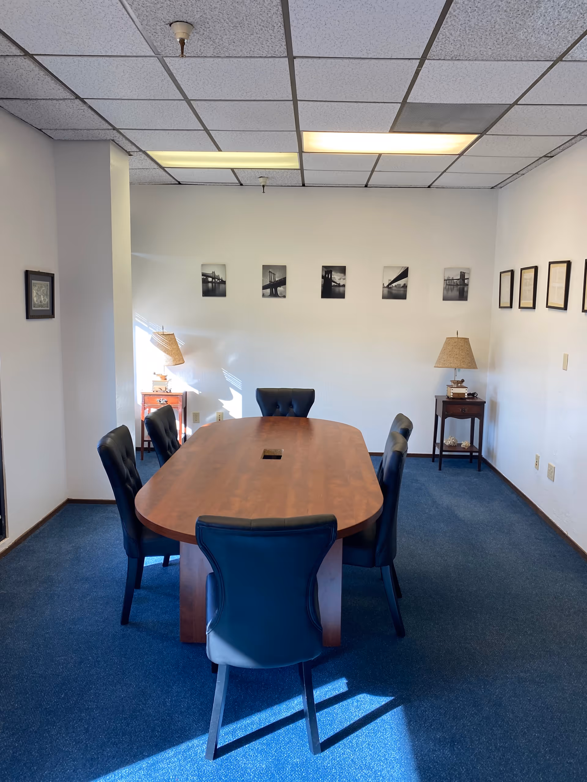A meeting room with an oval wooden table, six chairs, and framed artwork along walls.