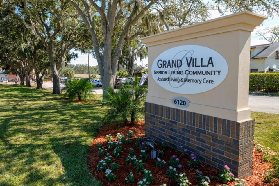 Exterior view of Grand Villa sign with landscaping and parking in the background.