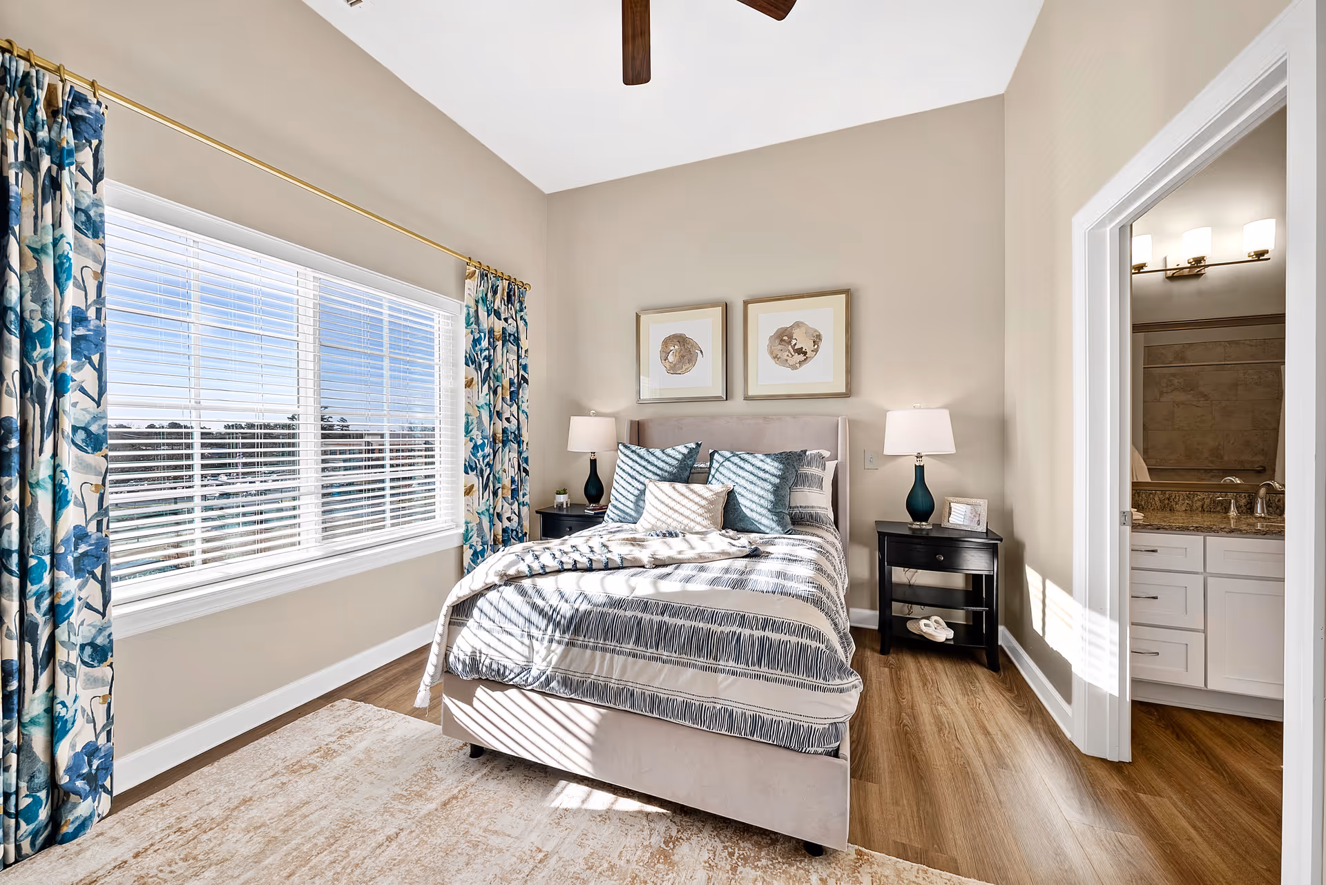 Bright bedroom in Meridian at Carolina Lakes with a bed, lamps, window, curtains, and adjoining bathroom.