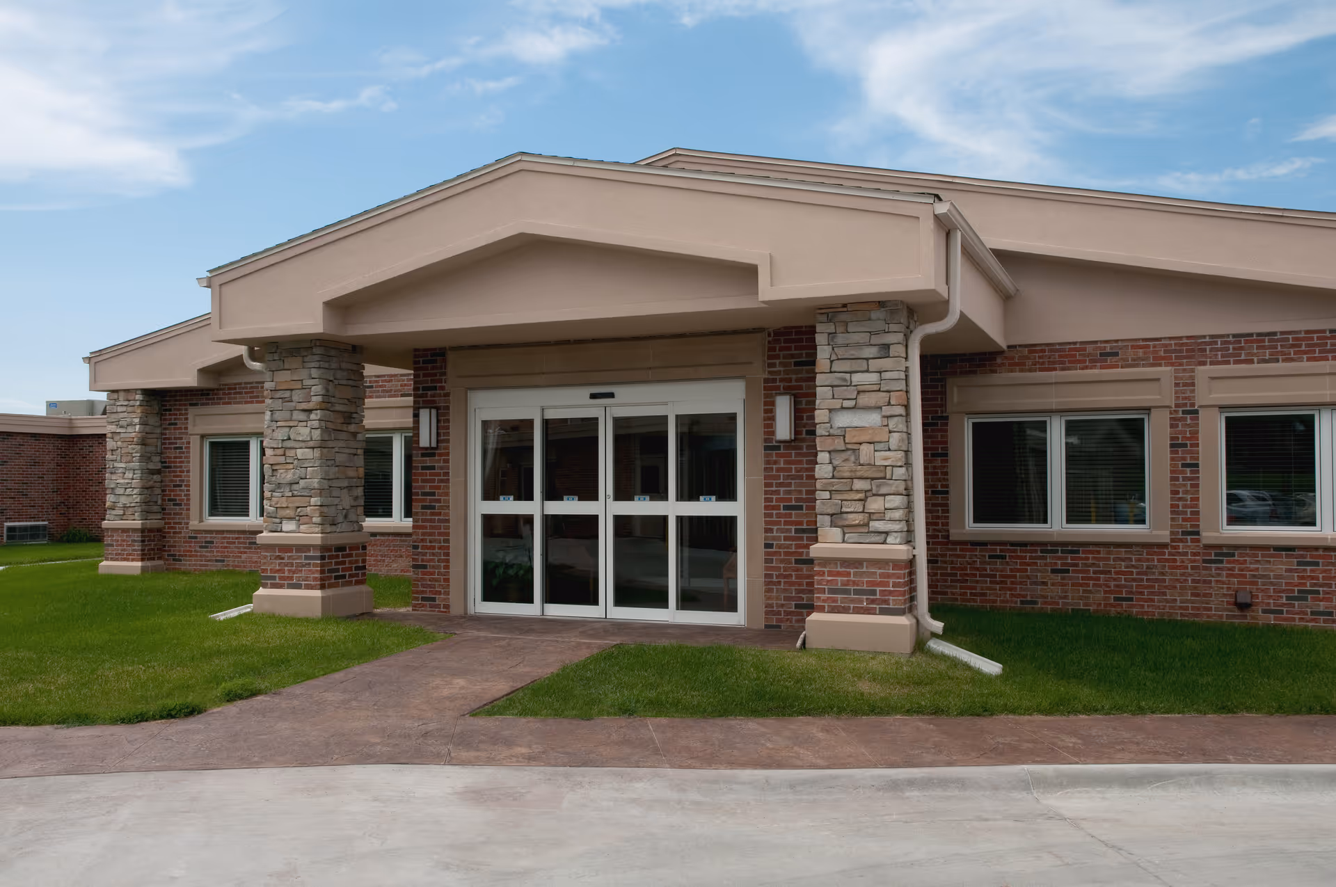 Front entrance of a single-story brick and stone building with a covered portico and automatic glass doors.