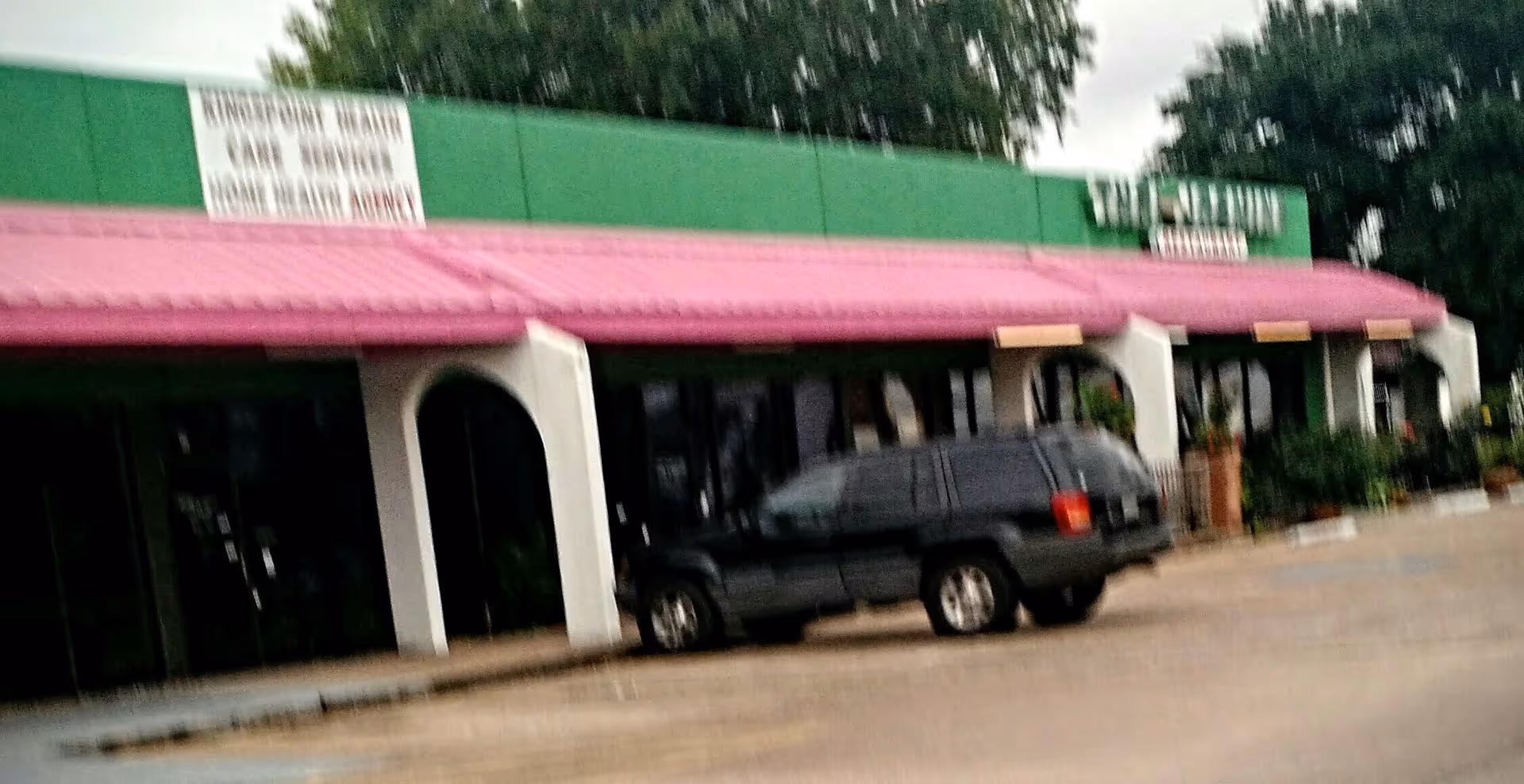 Front exterior of a building with a pink awning and a parked dark SUV.