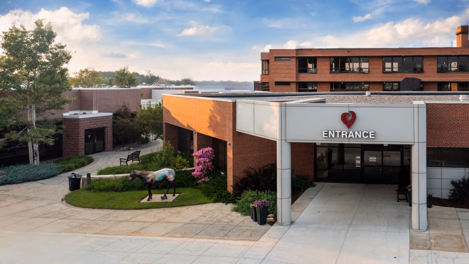 Exterior view of a brick hospital entrance at Sheridan Memorial Hospital, with sculpture and landscaped courtyard.