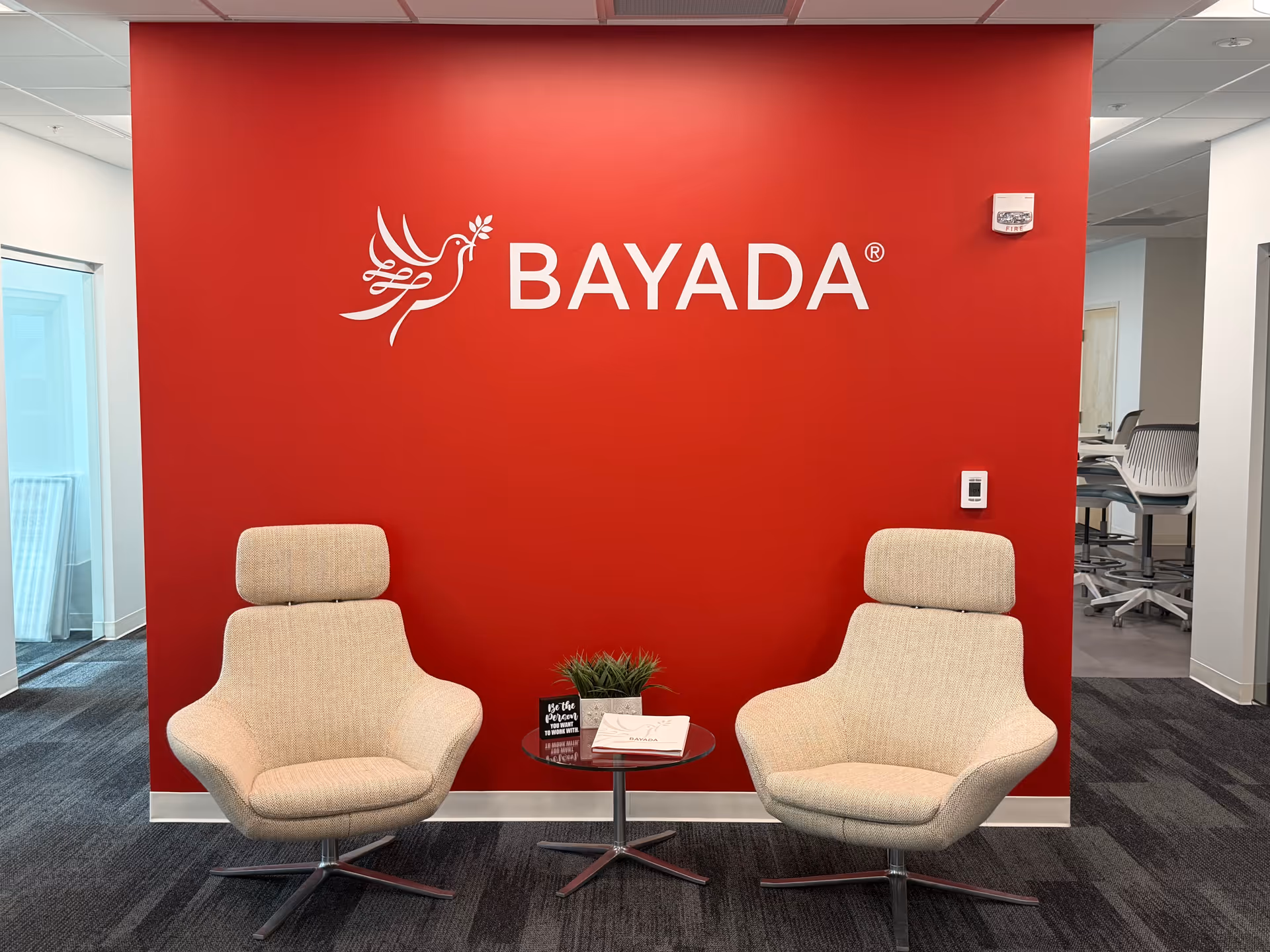 Two beige armchairs flank a small table in a BAYADA-branded red-walled lounge.