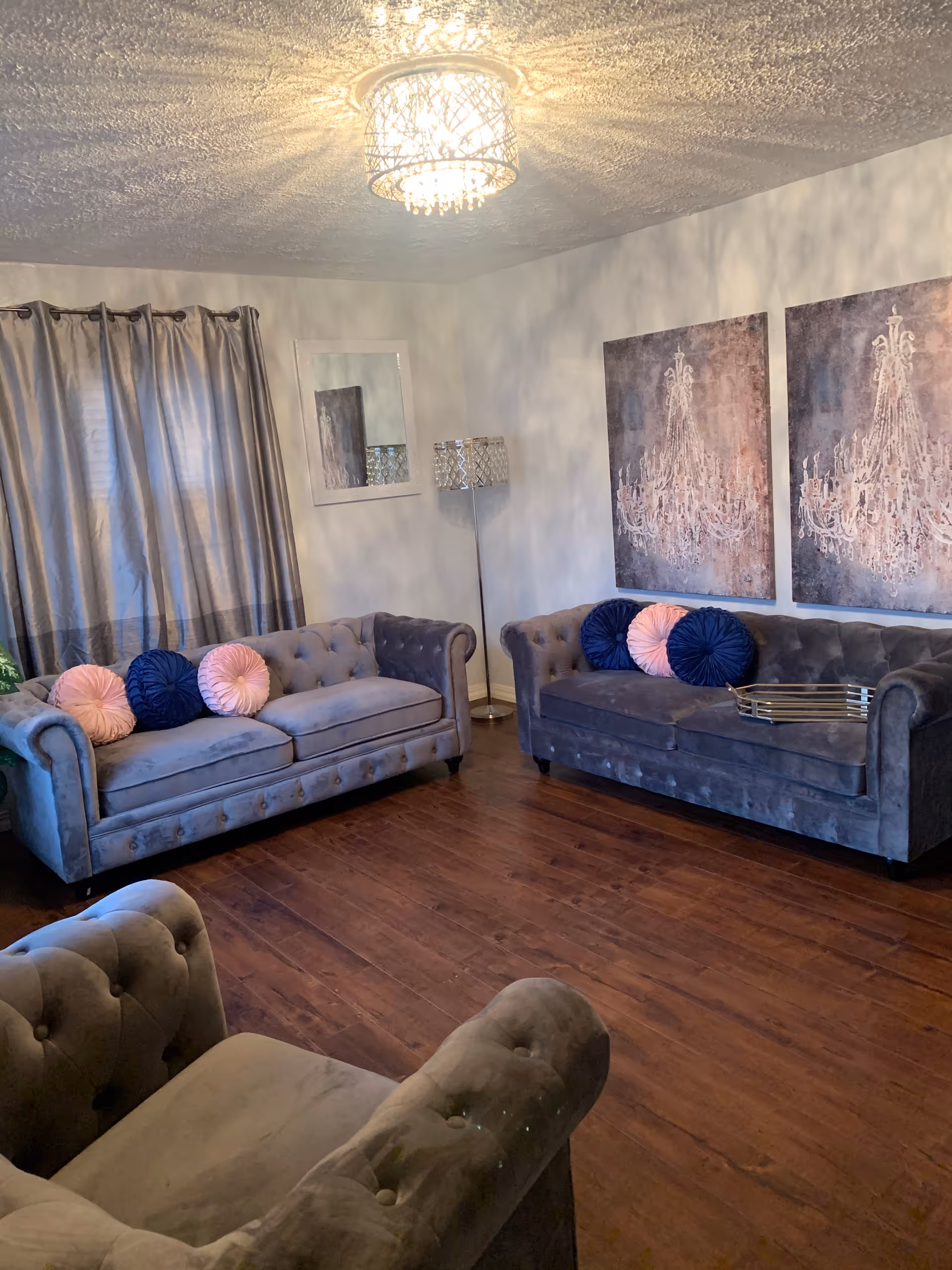 Living room inside the facility with tufted sofas, decorative pillows, chandelier, and wood floor.