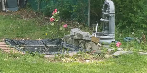 Outdoor garden area with a stone fountain, rocks, and pink flowers.