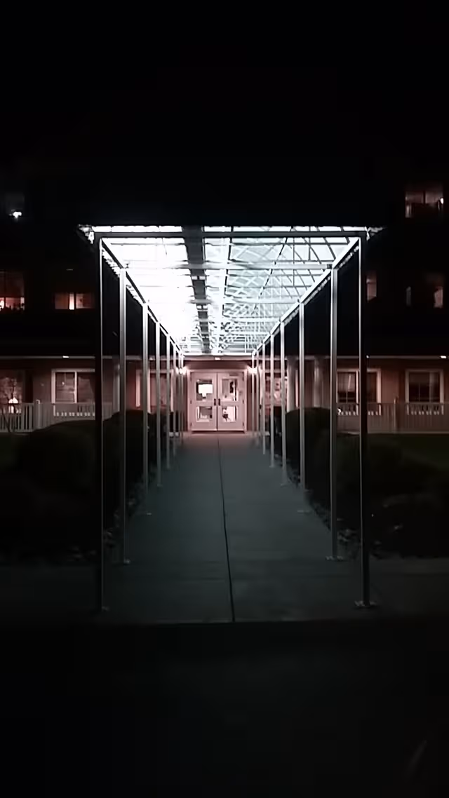 Night view of a lit covered outdoor walkway leading to a facility entrance.