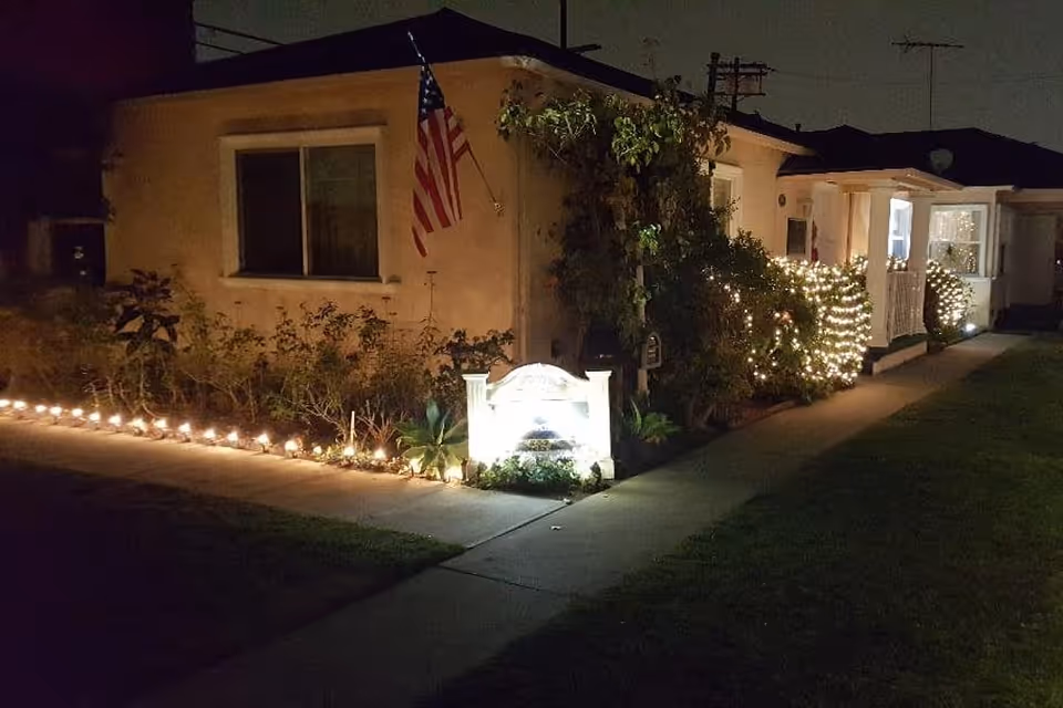 Night view of a single-story building front with a lit pathway, American flag and string lights decorating the shrubs.