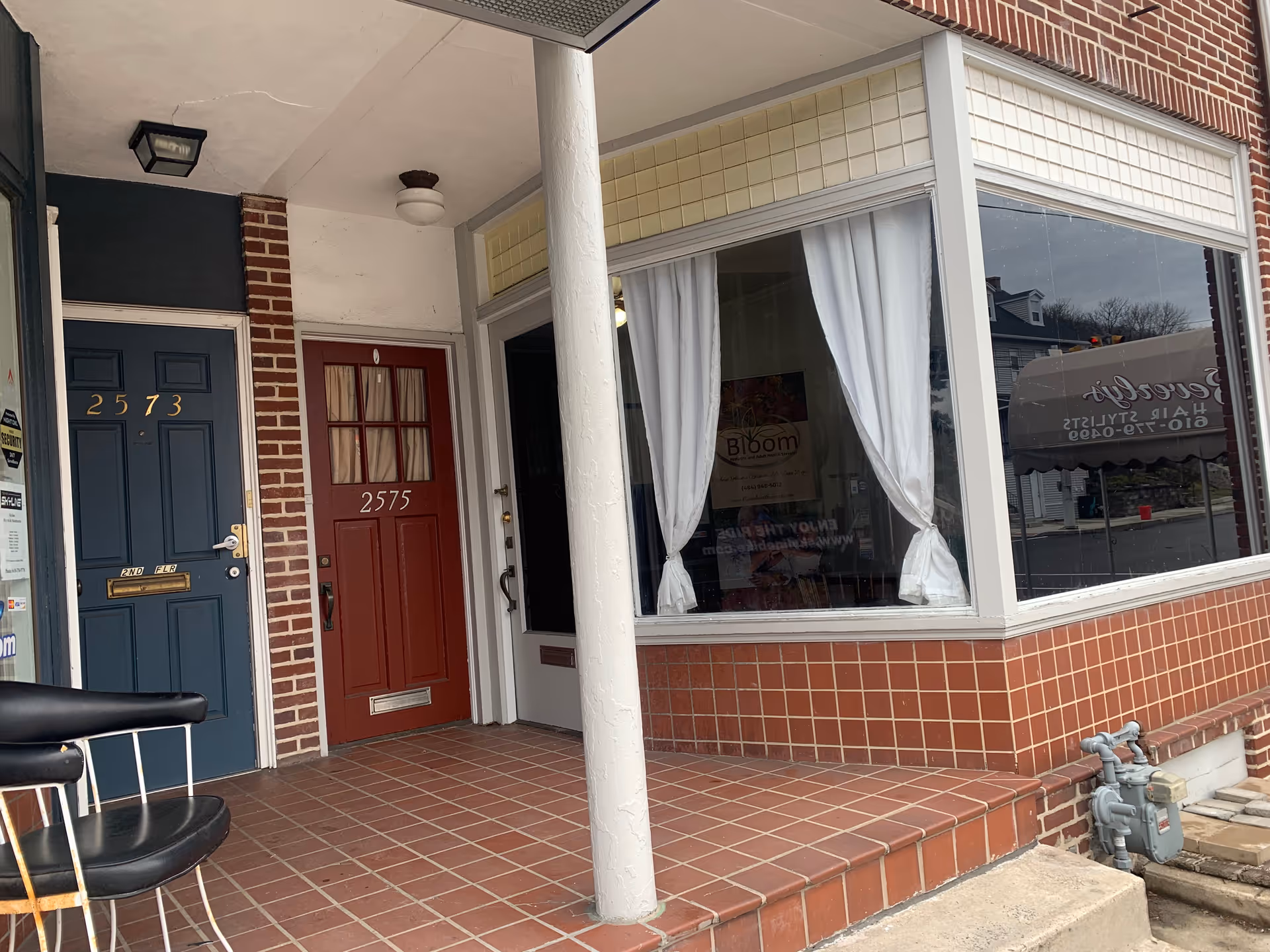 Brick storefront with blue and red doors and a window showing Bloom signage.