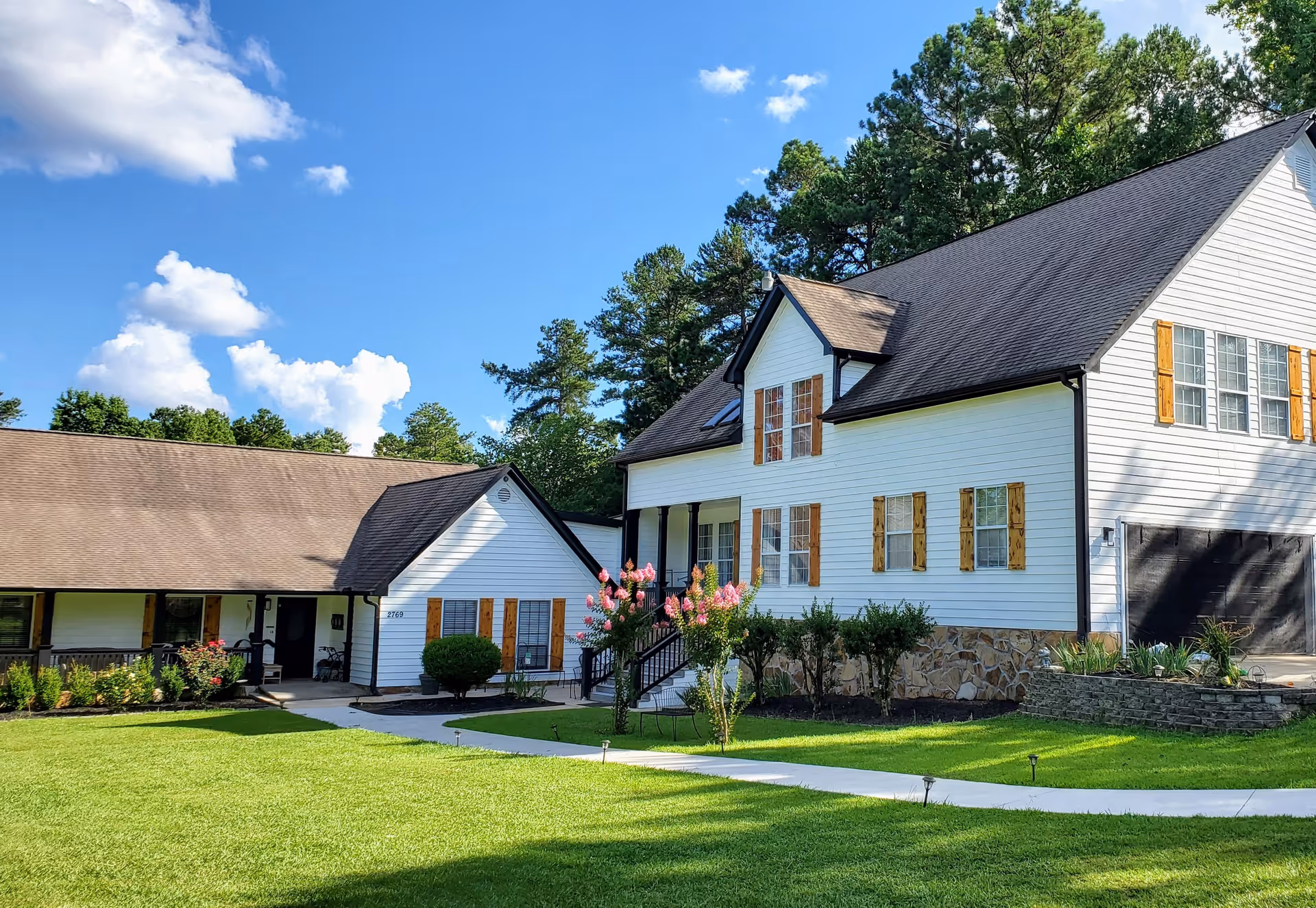 White, two-story senior living facility with a manicured lawn and blue sky.