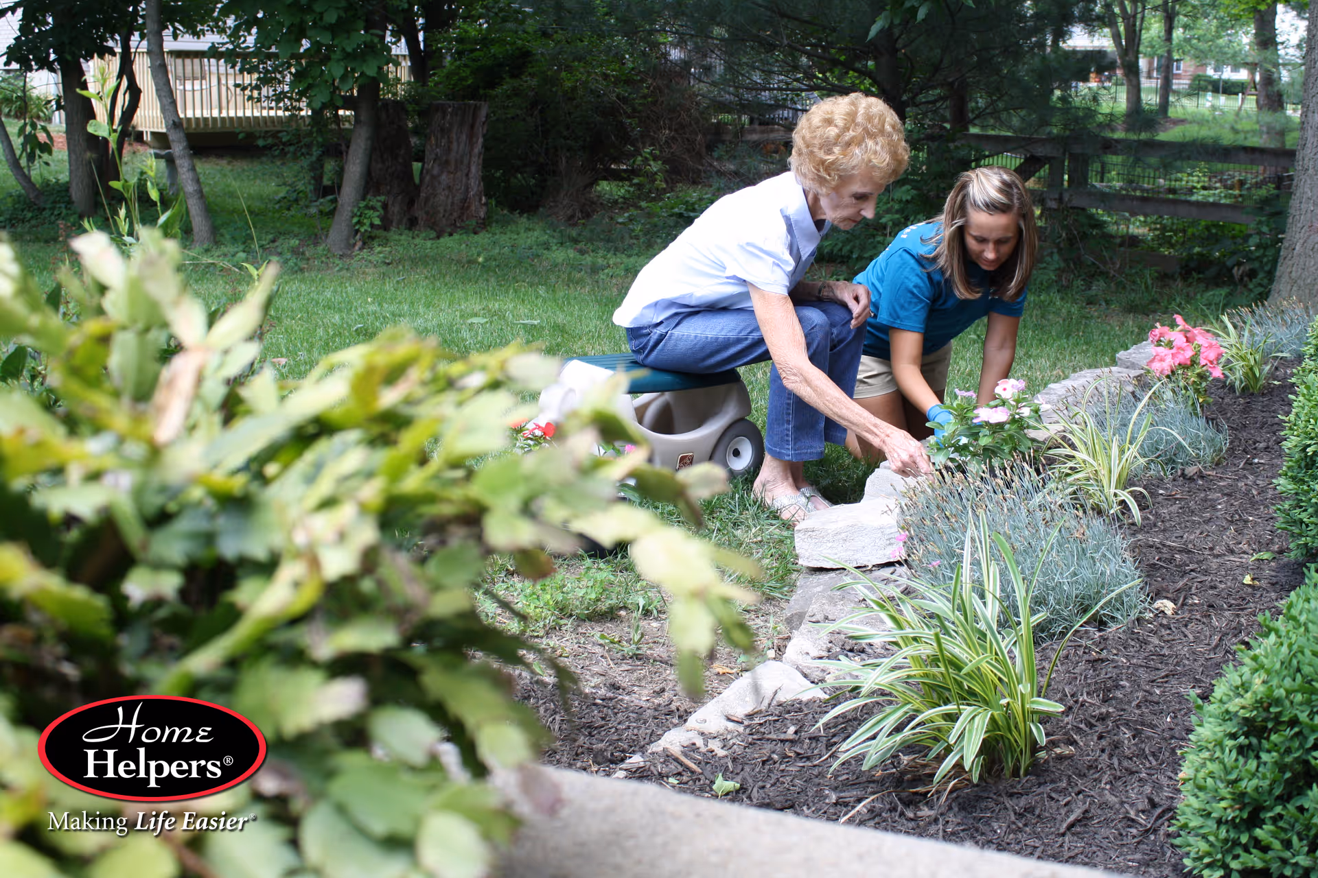 Two caregivers garden with an elderly resident outdoors in a sunny yard.