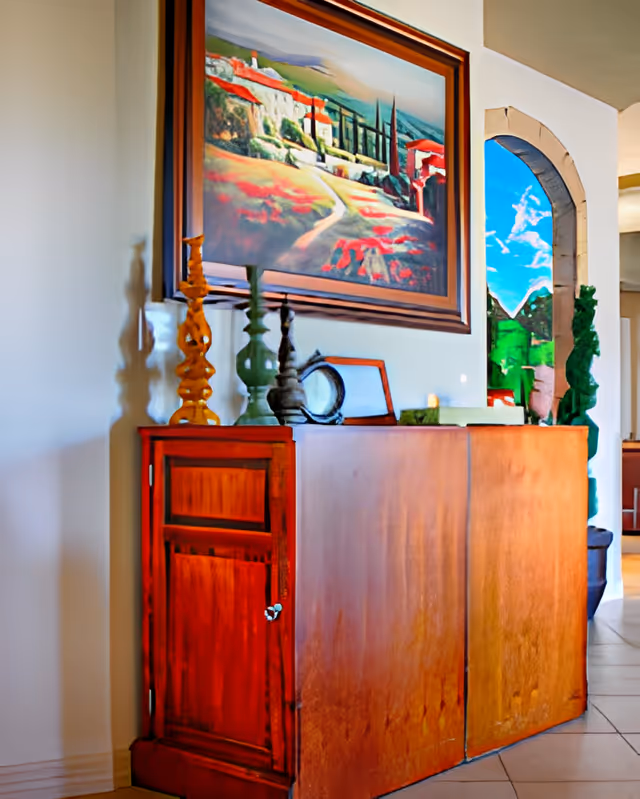 Wooden sideboard topped with decorative candlesticks and a framed landscape painting beside an arched doorway.