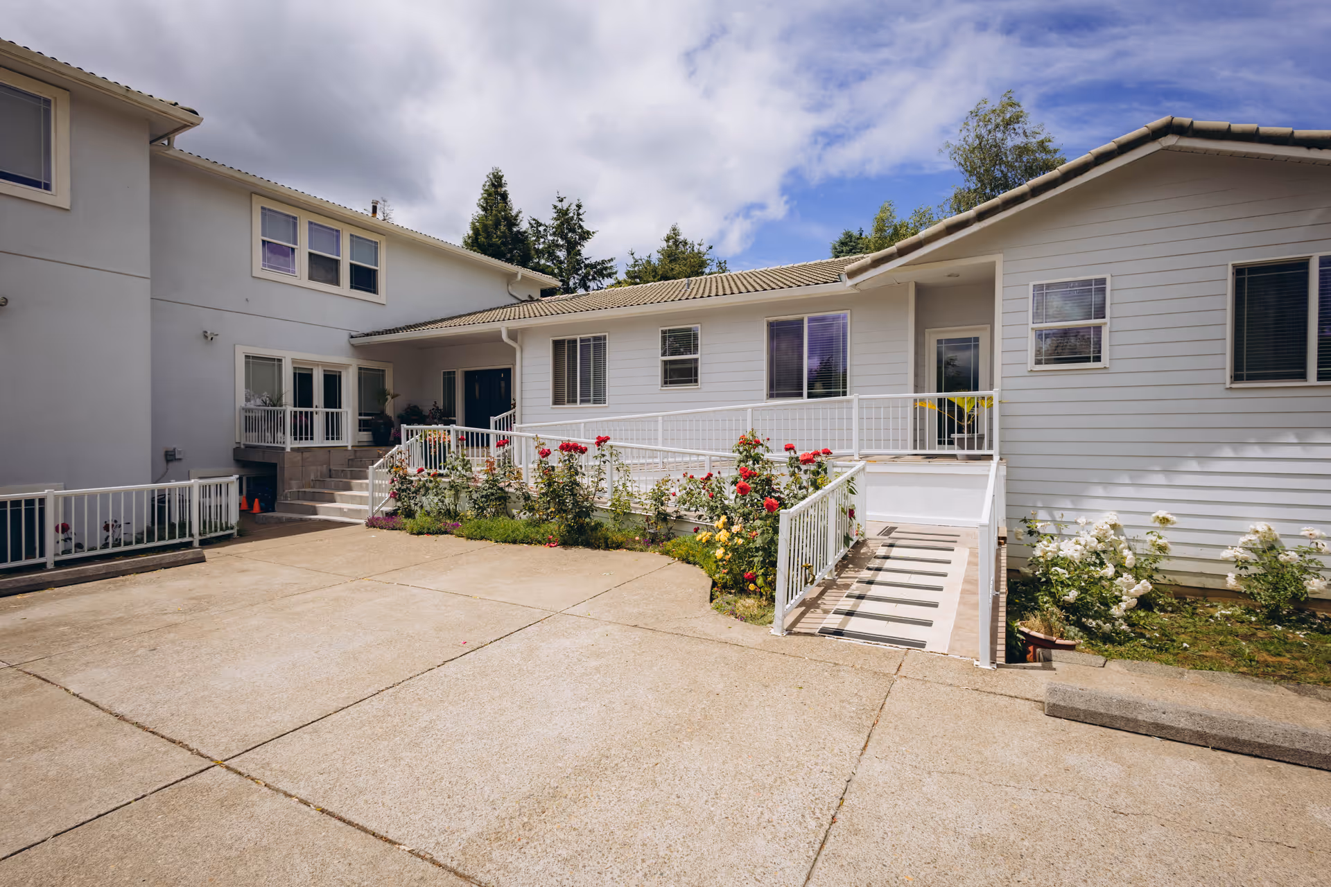 Exterior view of Happy Valley Graceful Living facility with white siding, garden roses, and a ramp.
