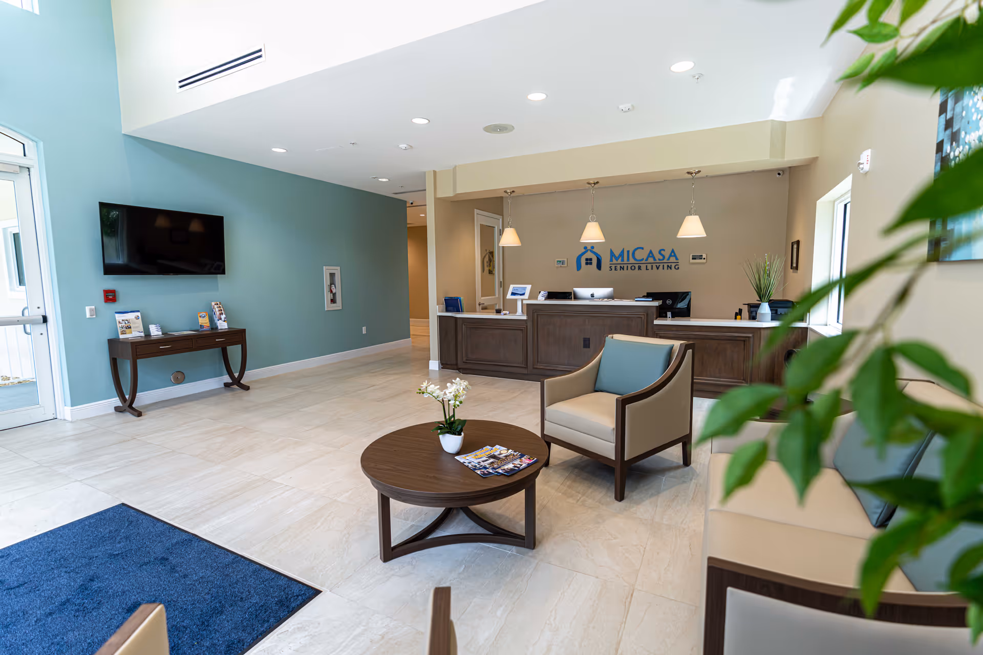 MiCasa Senior Living lobby with reception desk, seating area, TV, and potted plants.