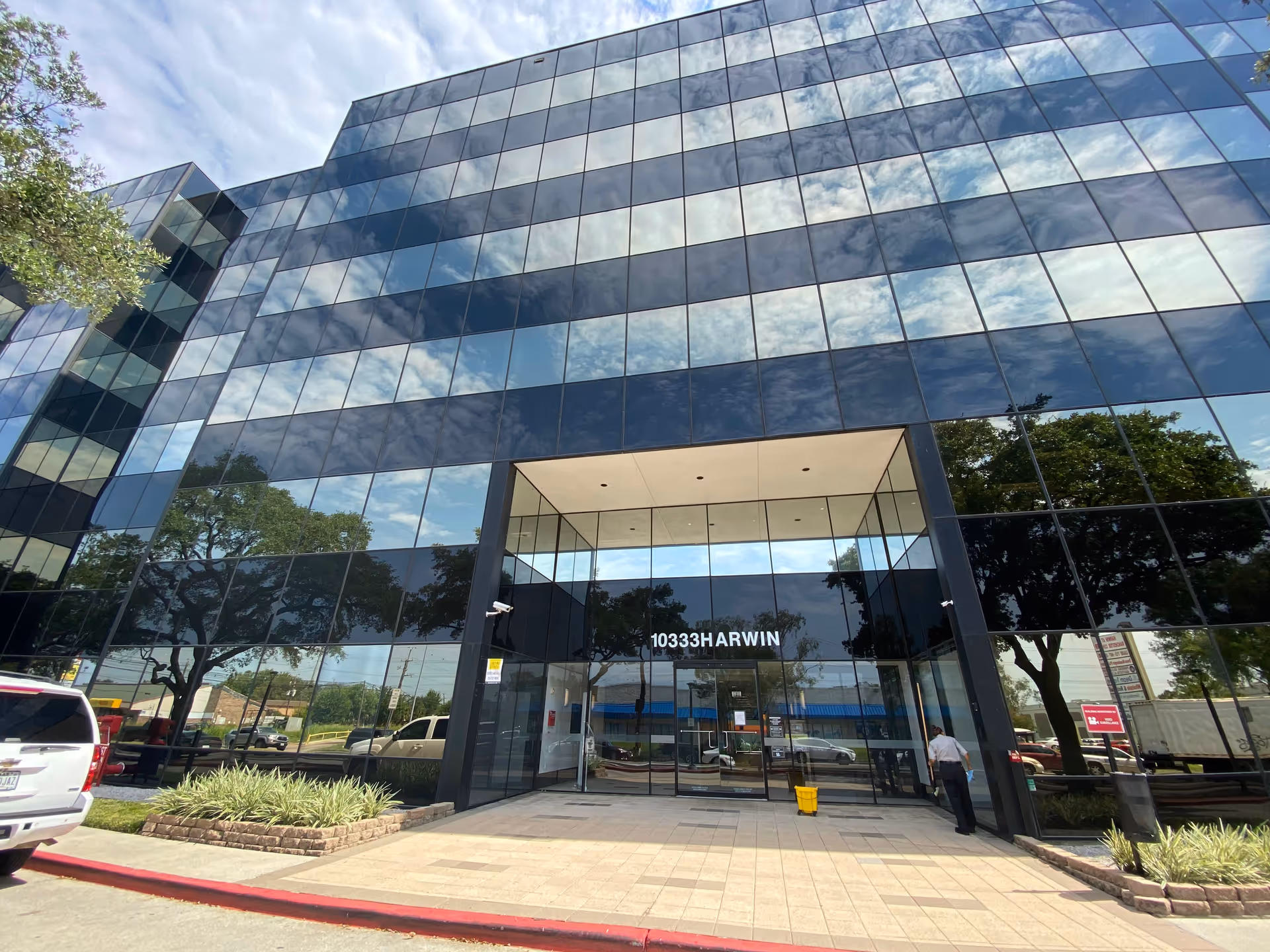 Glass-front facility exterior with a large entrance and reflections of trees and sky.