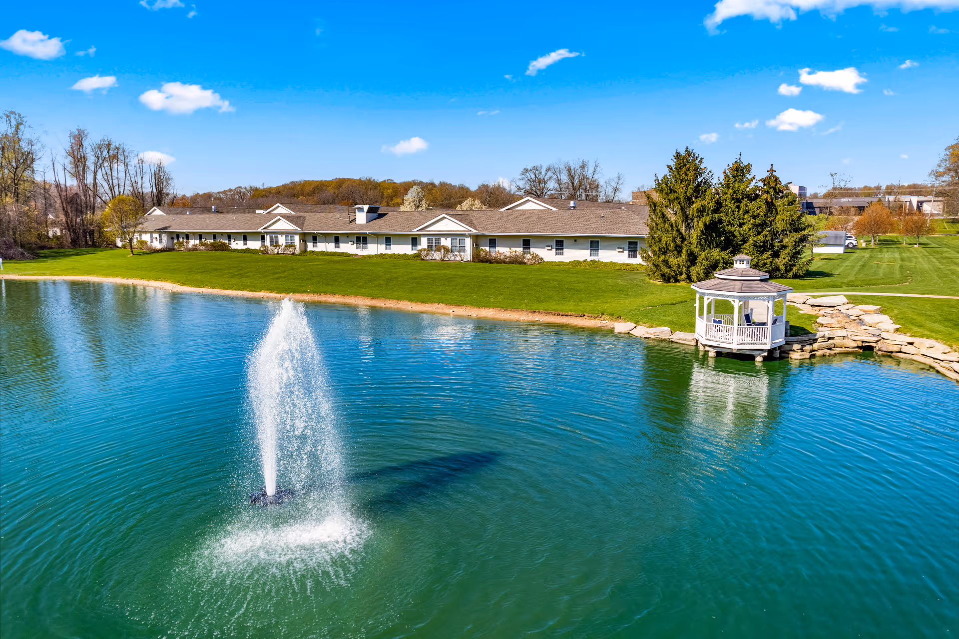 Pond-side senior living campus with fountain, gazebo, and manicured lawn.