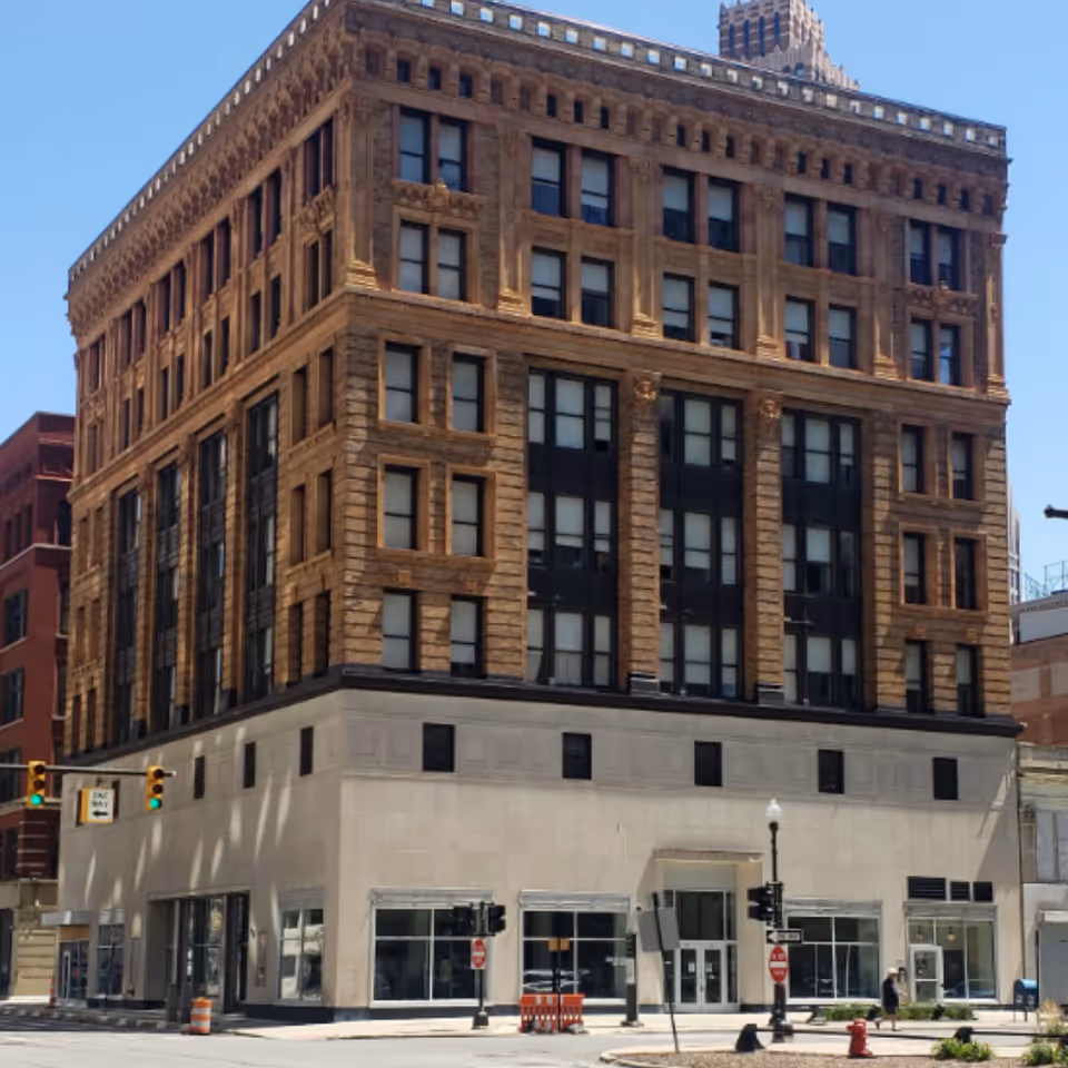 A tall brick urban building on a street corner with storefronts at ground level.