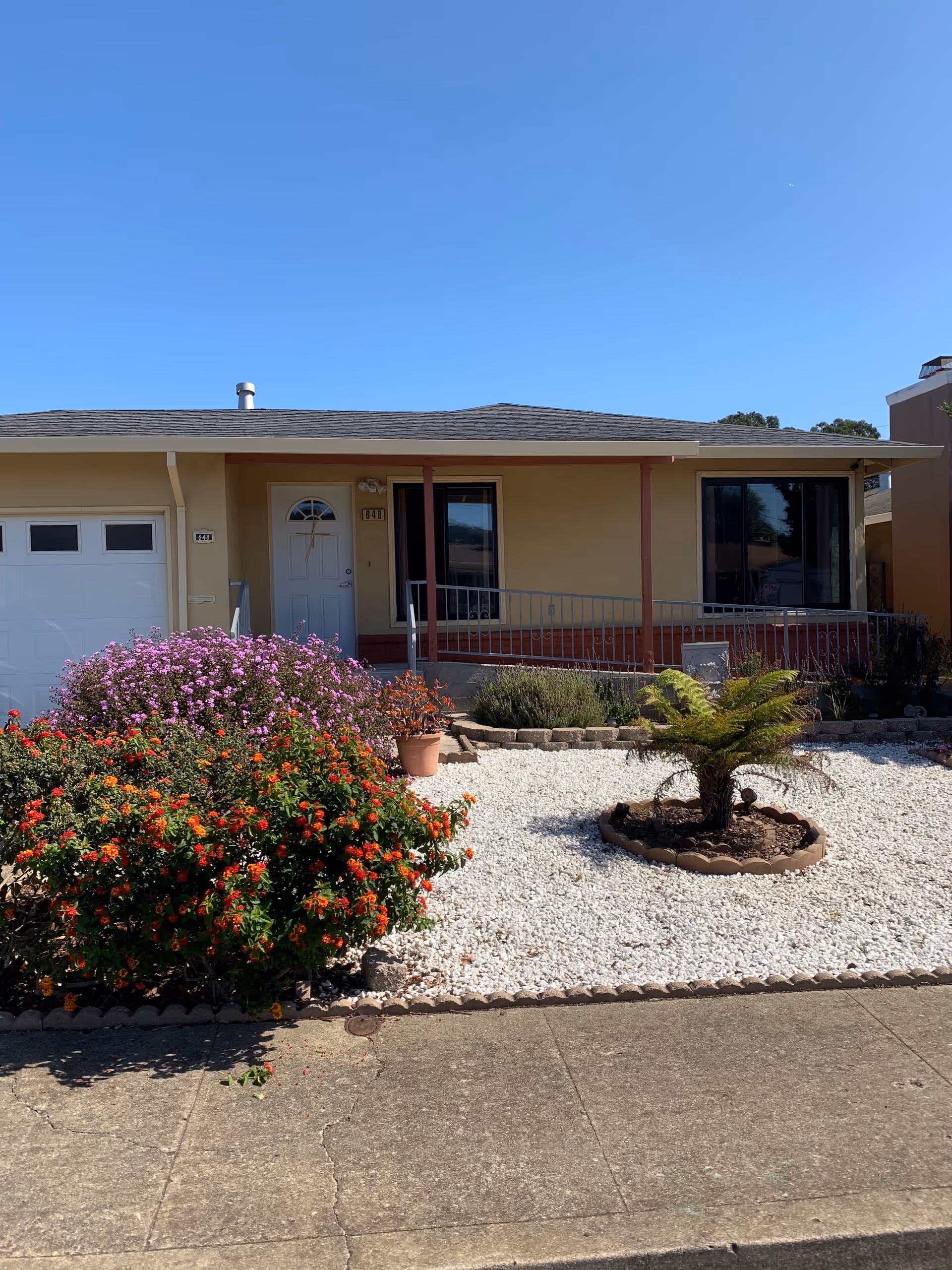 Front view of a single-story beige building with a small garden and white gravel yard.