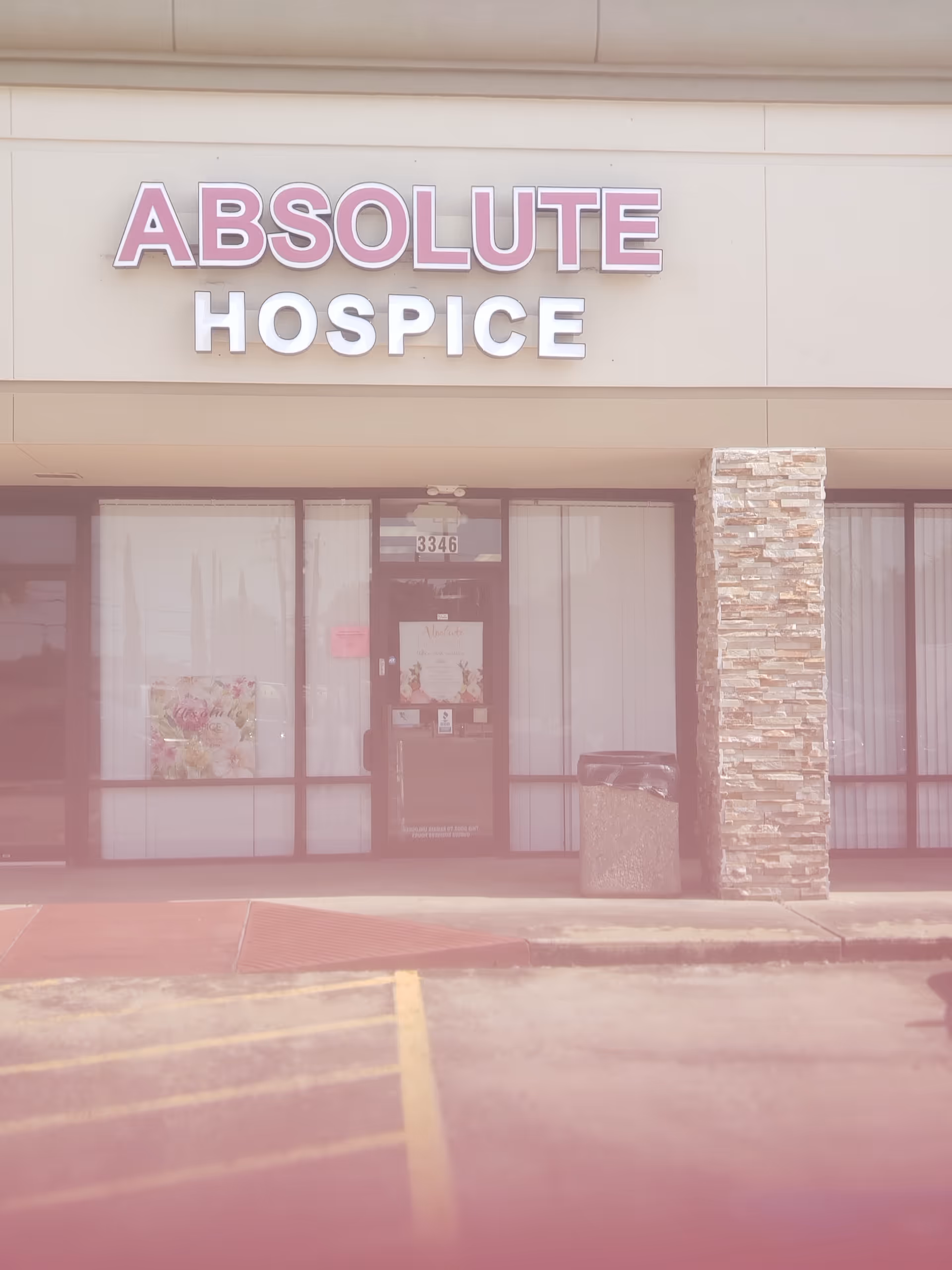 Exterior view of Absolute Hospice storefront with glass doors and a stone pillar.
