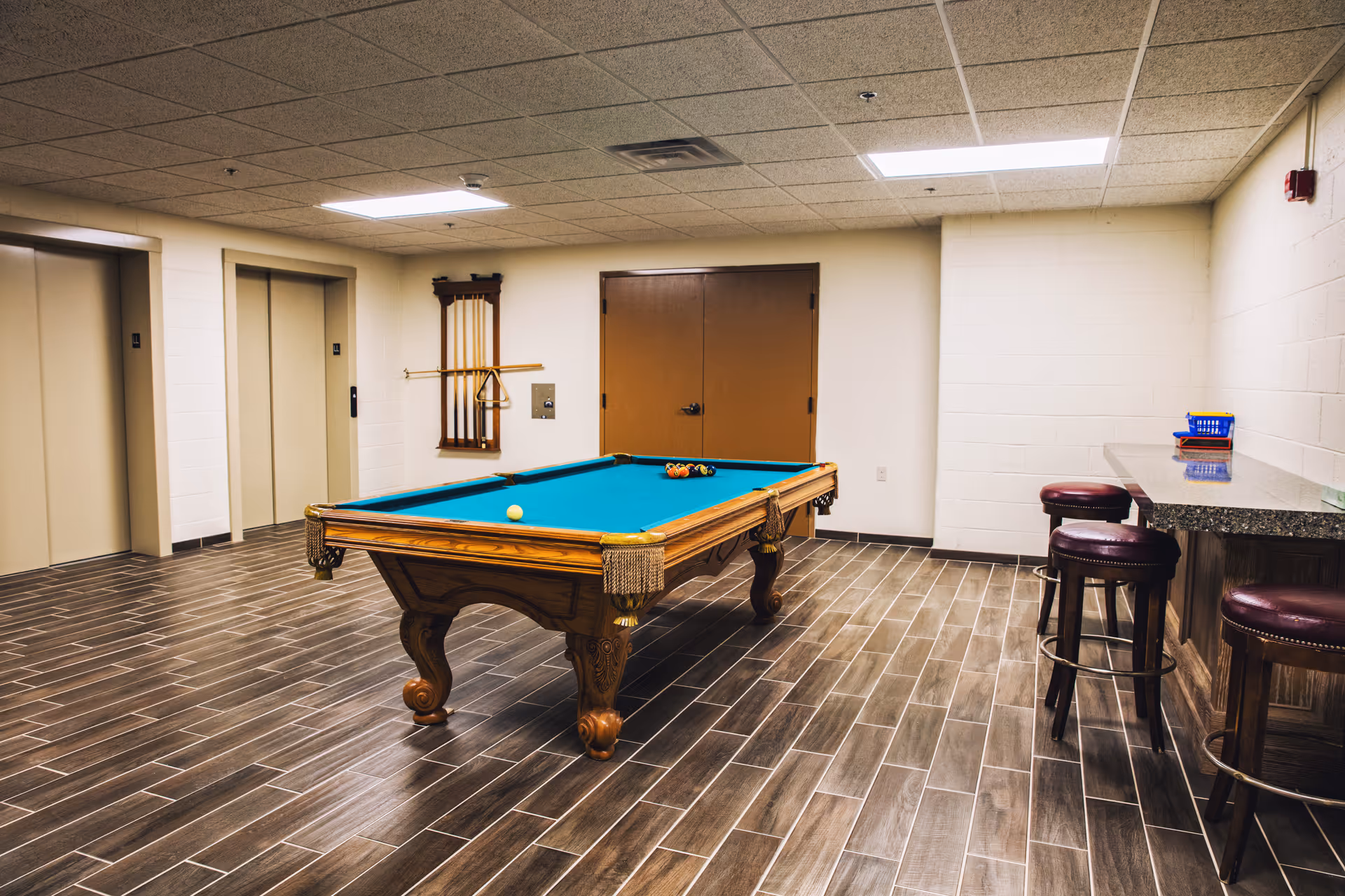 Interior recreation room with a pool table, wall rack, and bar stools in senior living facility
