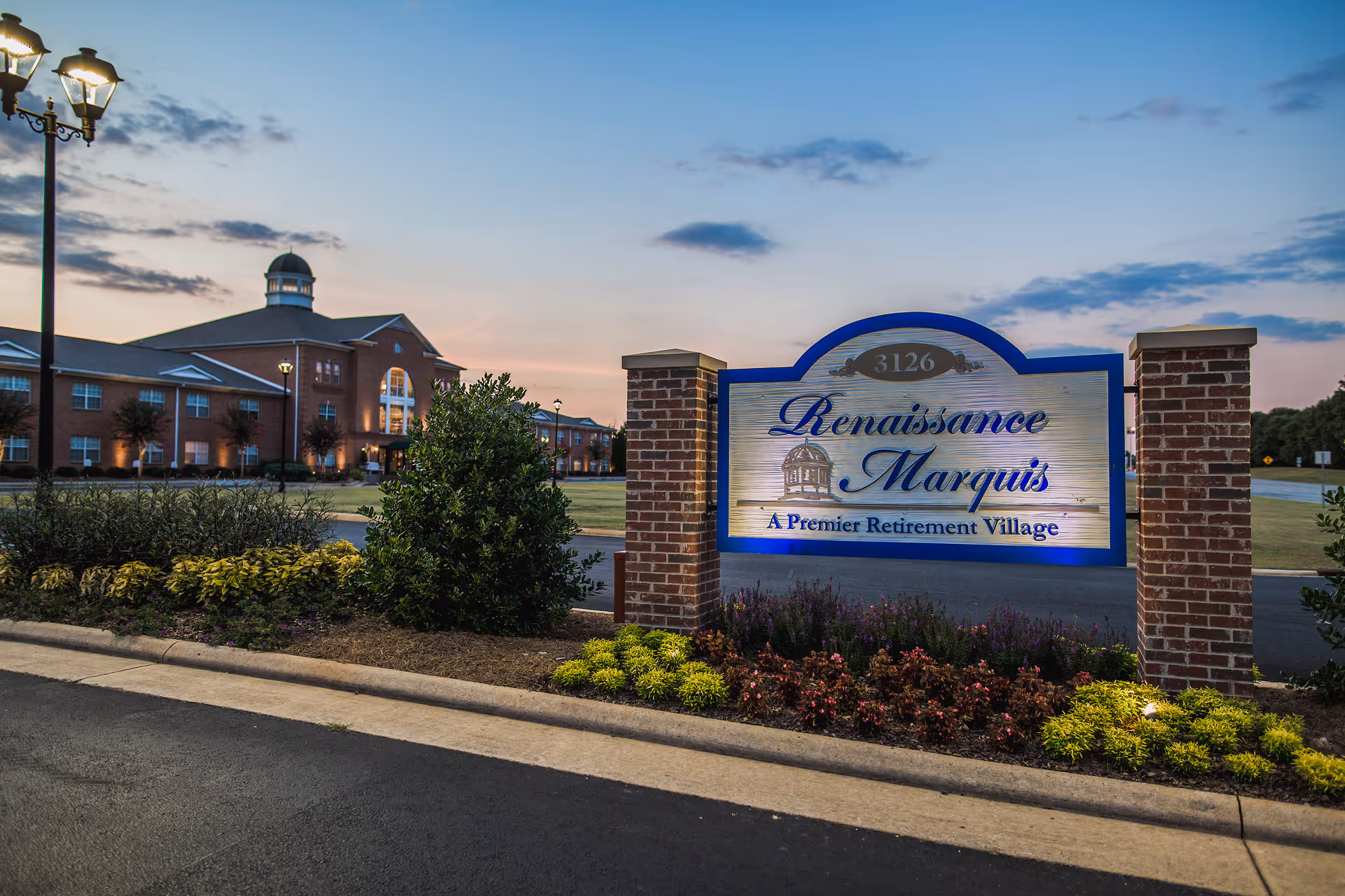 Illuminated sign reading 'Renaissance Marquis — A Premier Retirement Village' in front of a brick senior living building at dusk.