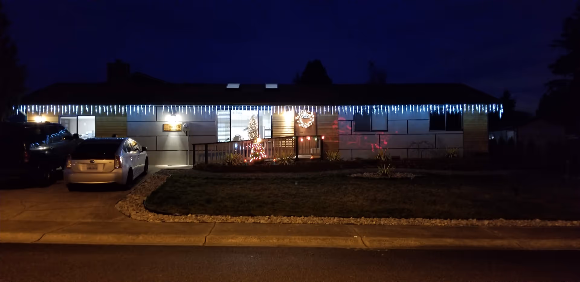 Night exterior of BEMA PEACE CARE Adult Family Home with icicle lights and two parked cars.