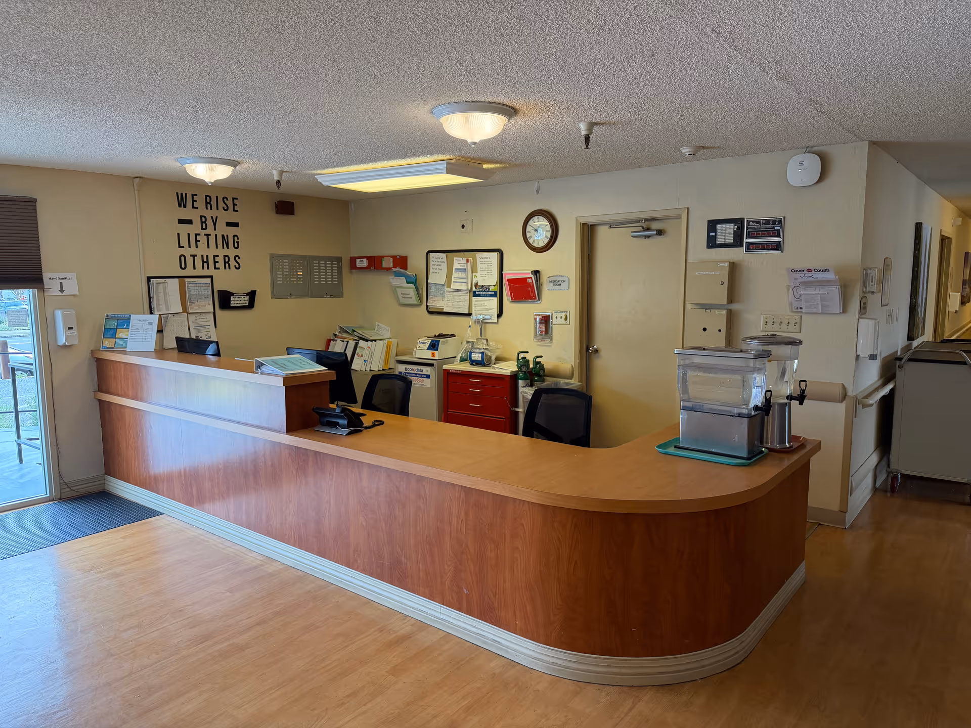 Lobby reception desk with paperwork, notices, and a beverage dispenser in a nursing facility.