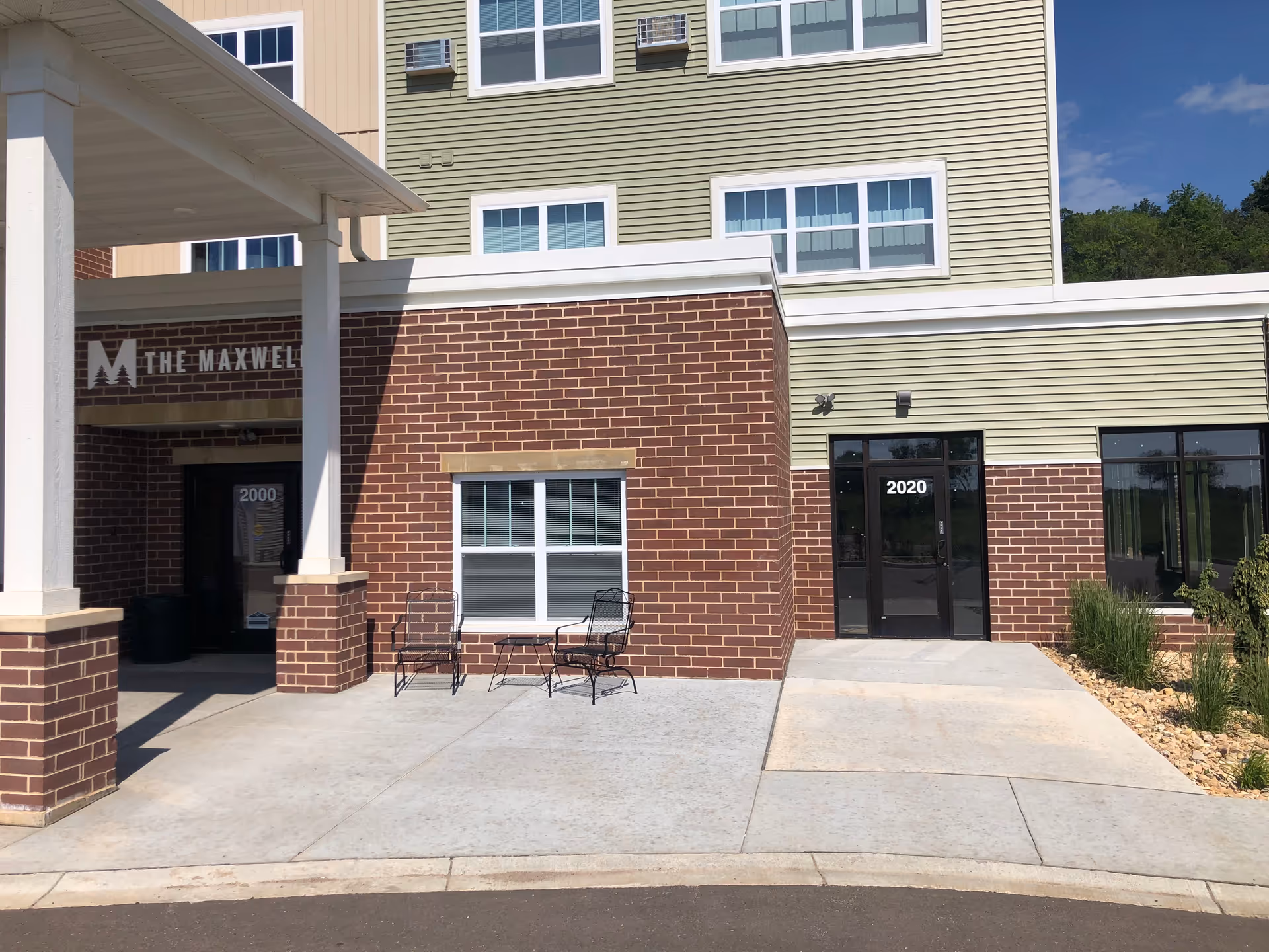 The Maxwell senior living facility exterior with brick facade, signage, and outdoor seating.