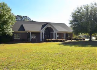 Front view of Jubilee Gardens Senior Living, a brick, single-story building with arched entrance and lawn.