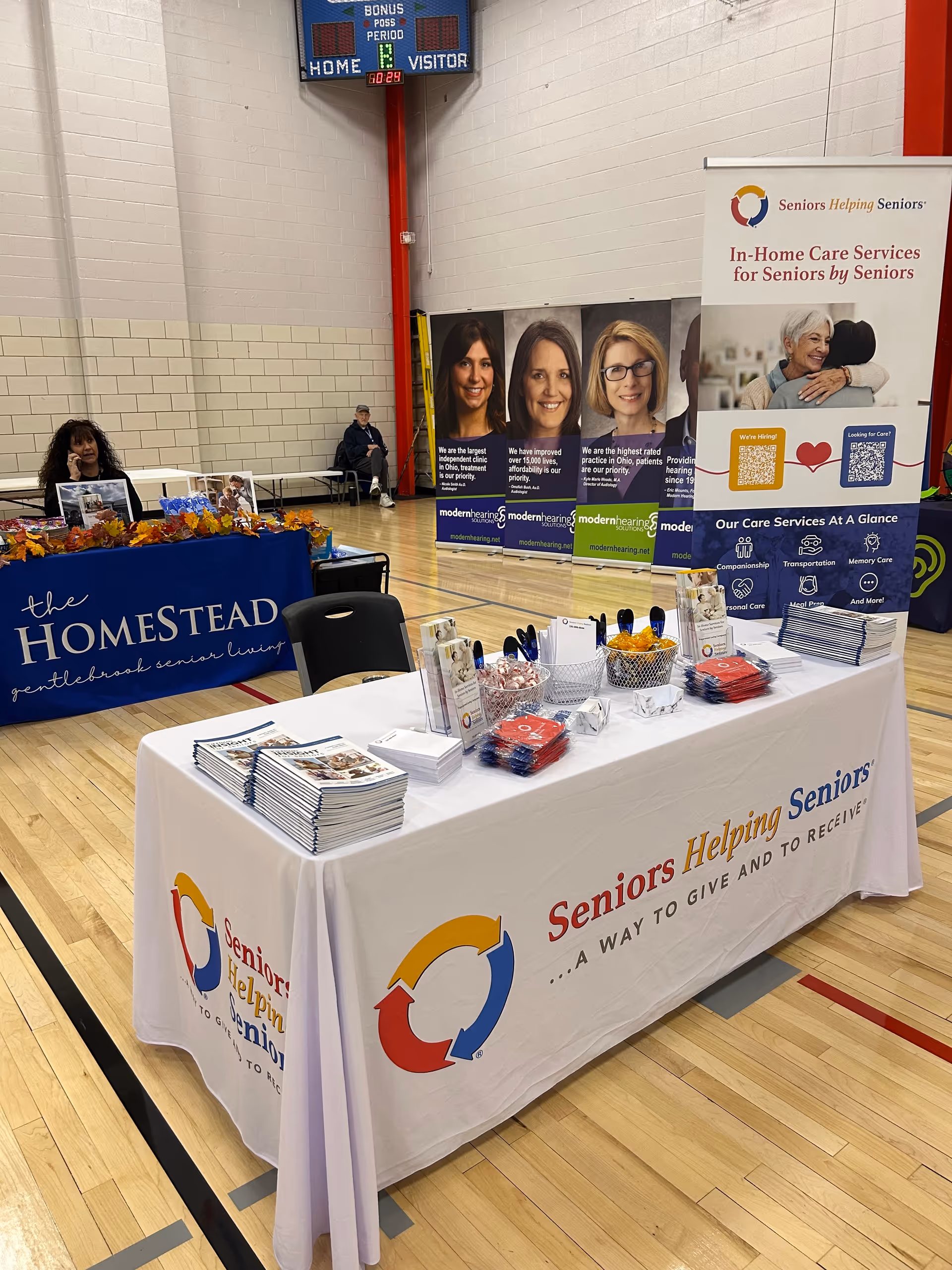 Indoor gym hosting a senior services fair with booths, banners, and tables.