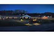 Nighttime exterior view of Elkins Rehabilitation and Care Center with lit windows and parked cars.