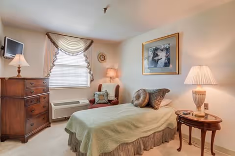 Cozy senior living bedroom with bed, dresser, window, and bedside lamps.