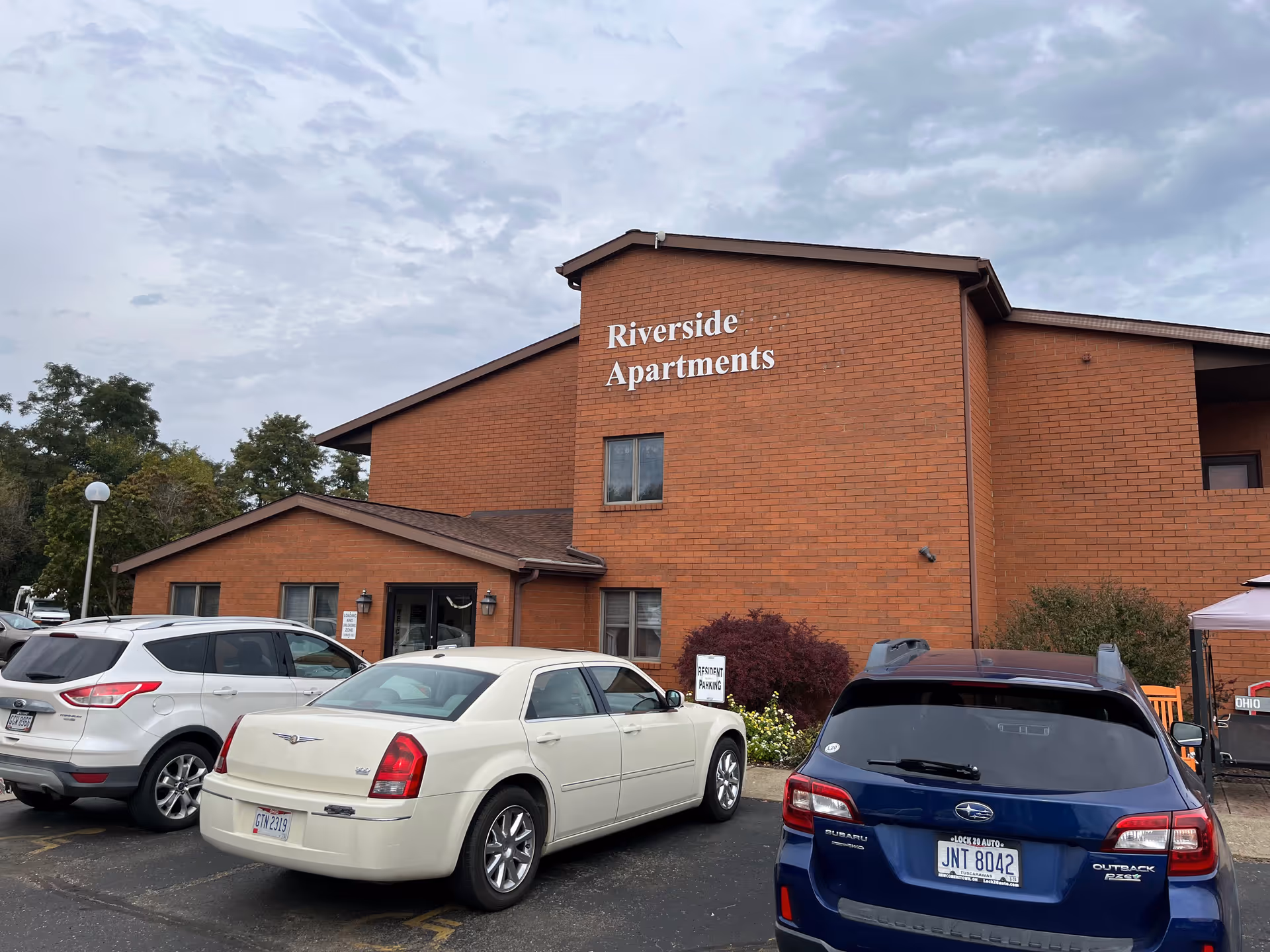 Brick Riverside Apartments building with several cars parked in front.