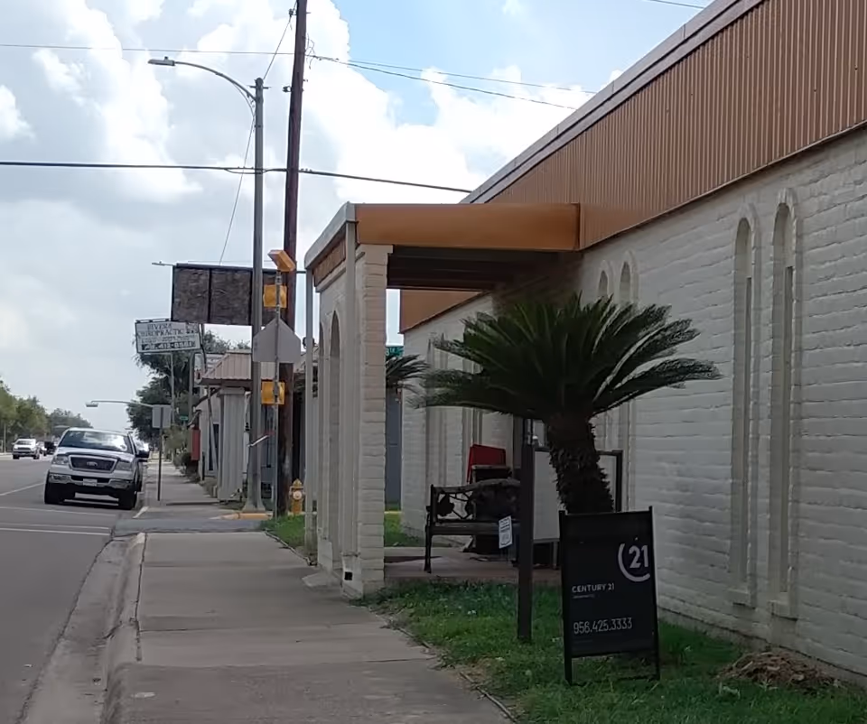 Street view of a white brick building with arches, palm tree, and Century 21 sign.