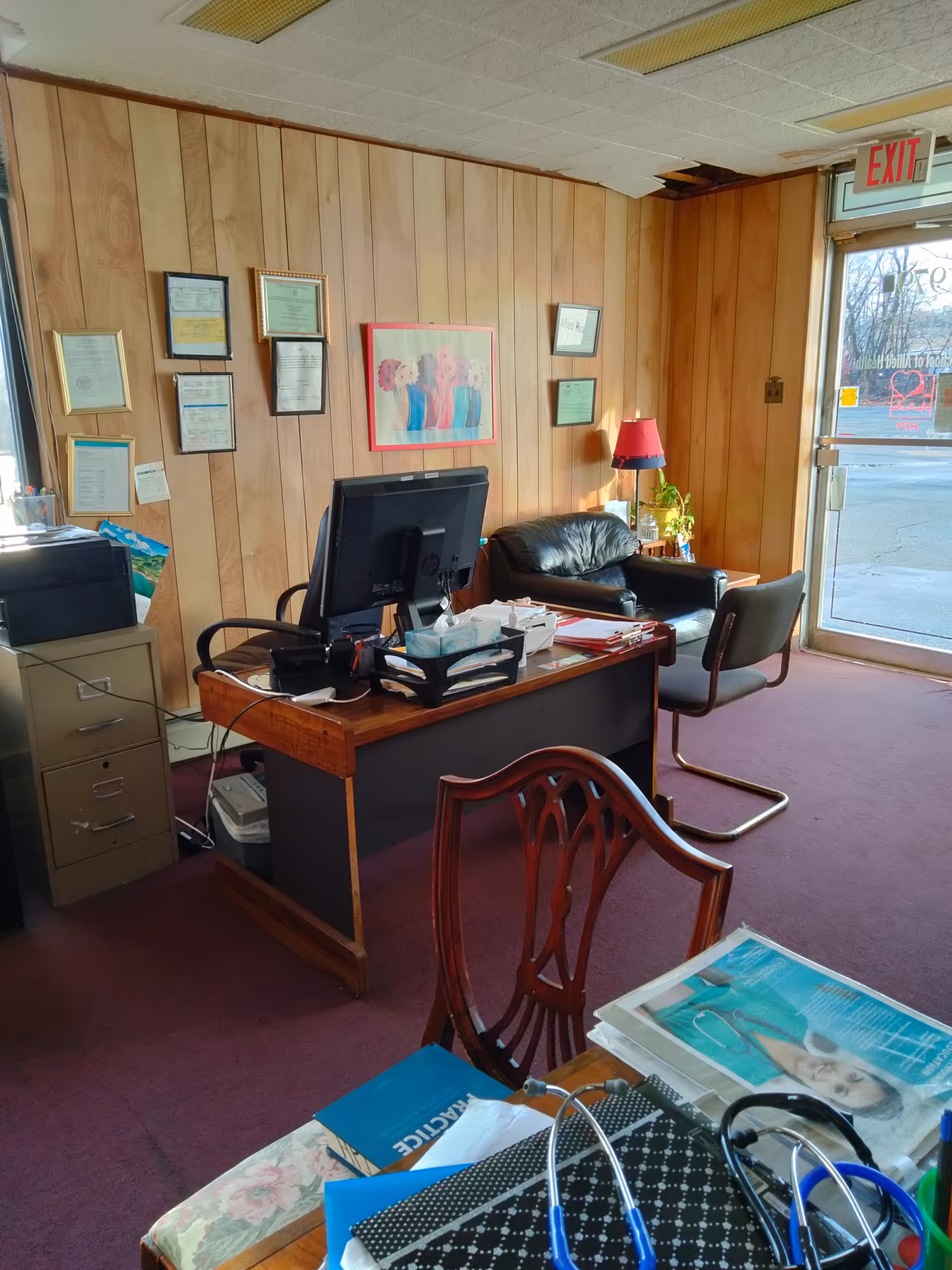 Office workspace with computer, documents, and certificates on wood-paneled walls.
