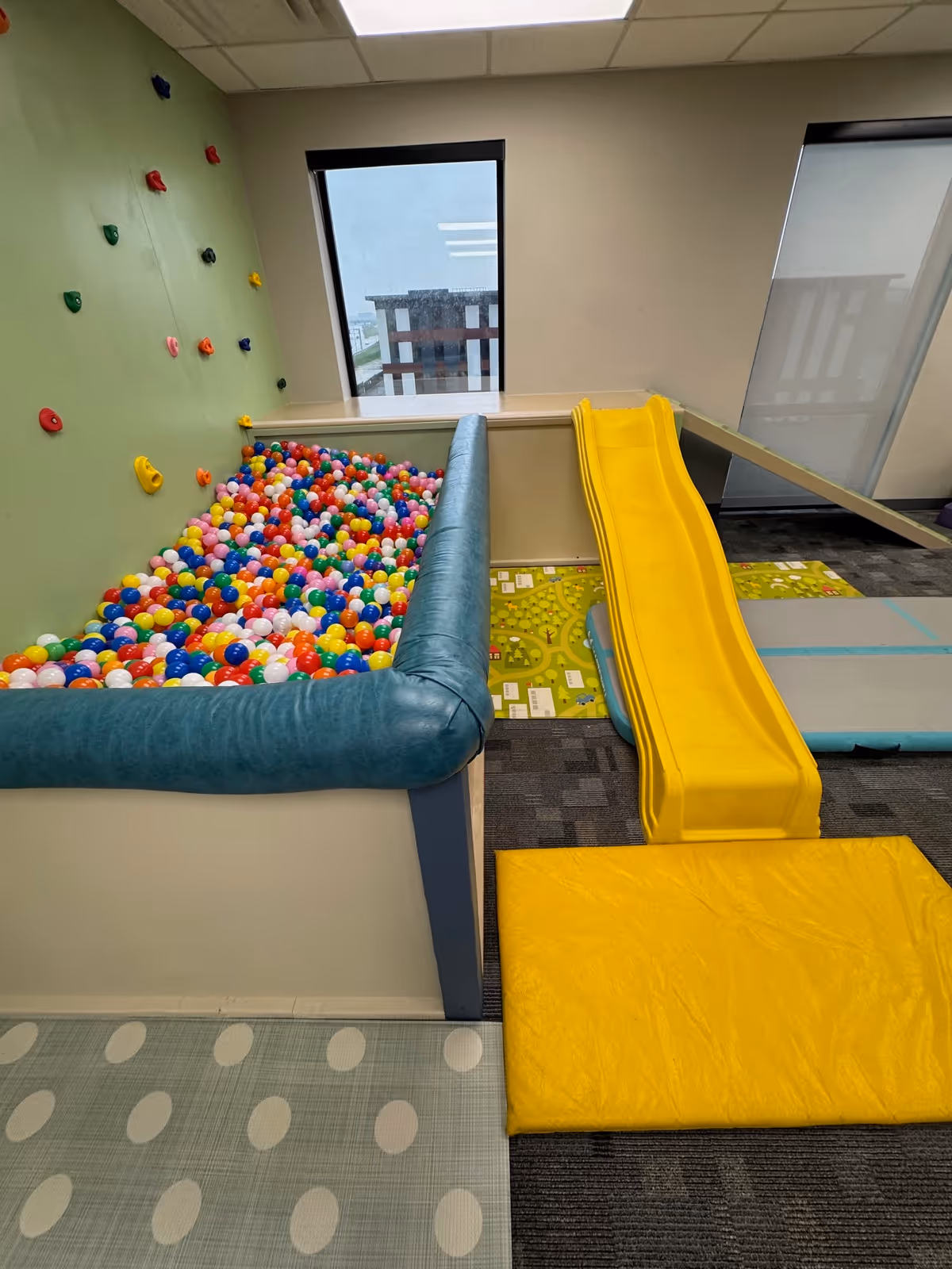 Colorful ball pit with climbing wall and yellow slide inside a children's play area.